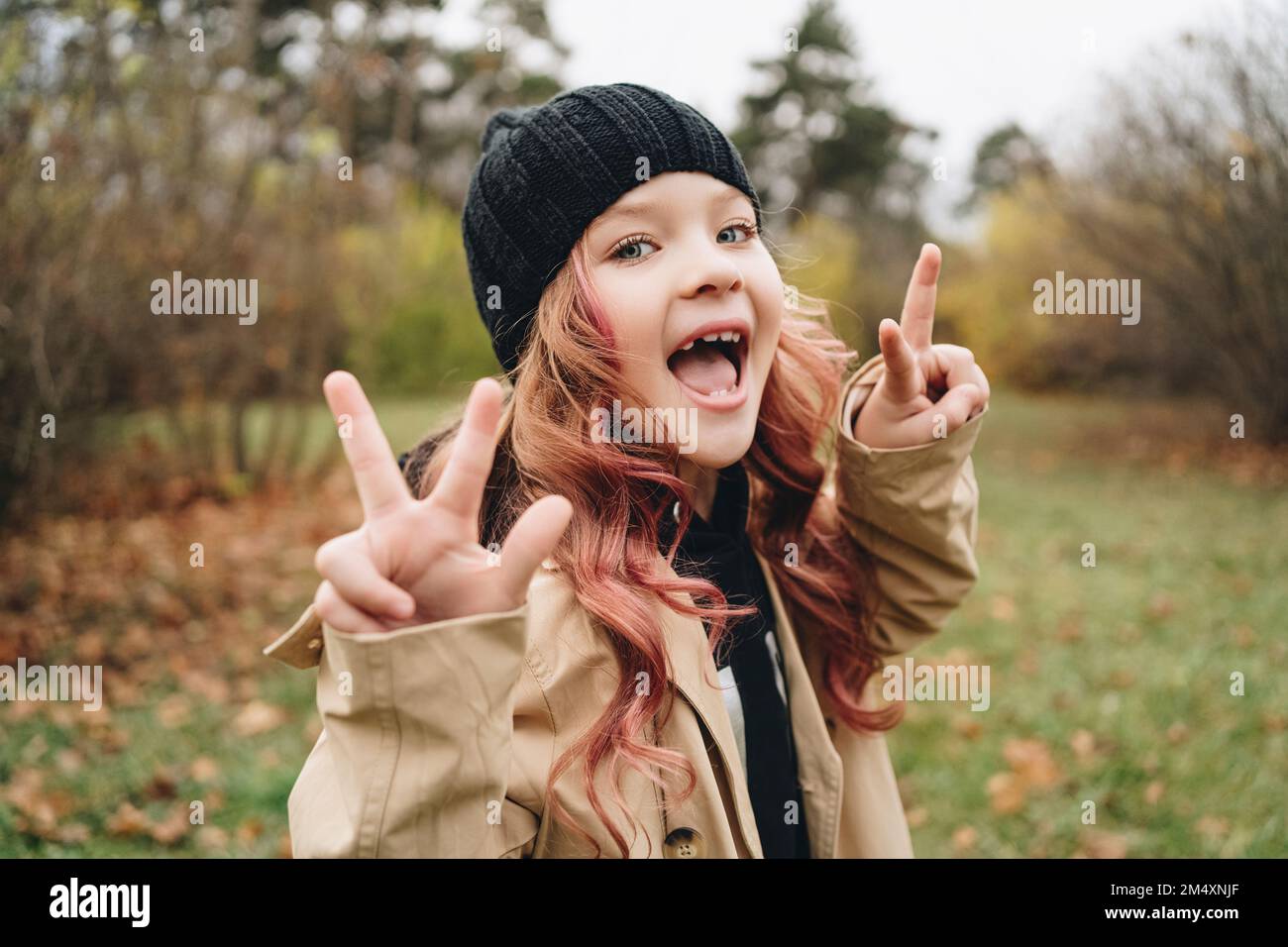 Fille gaie portant un chapeau en tricot montrant le signe de paix geste dans le parc Banque D'Images