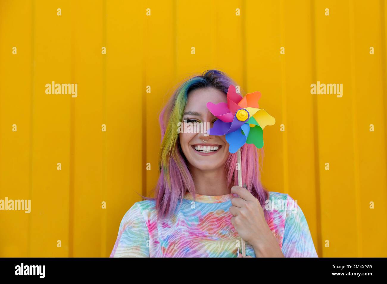 Une femme heureuse portant un t-shirt teint par cravate tenant un jouet à volant coloré devant un mur jaune Banque D'Images