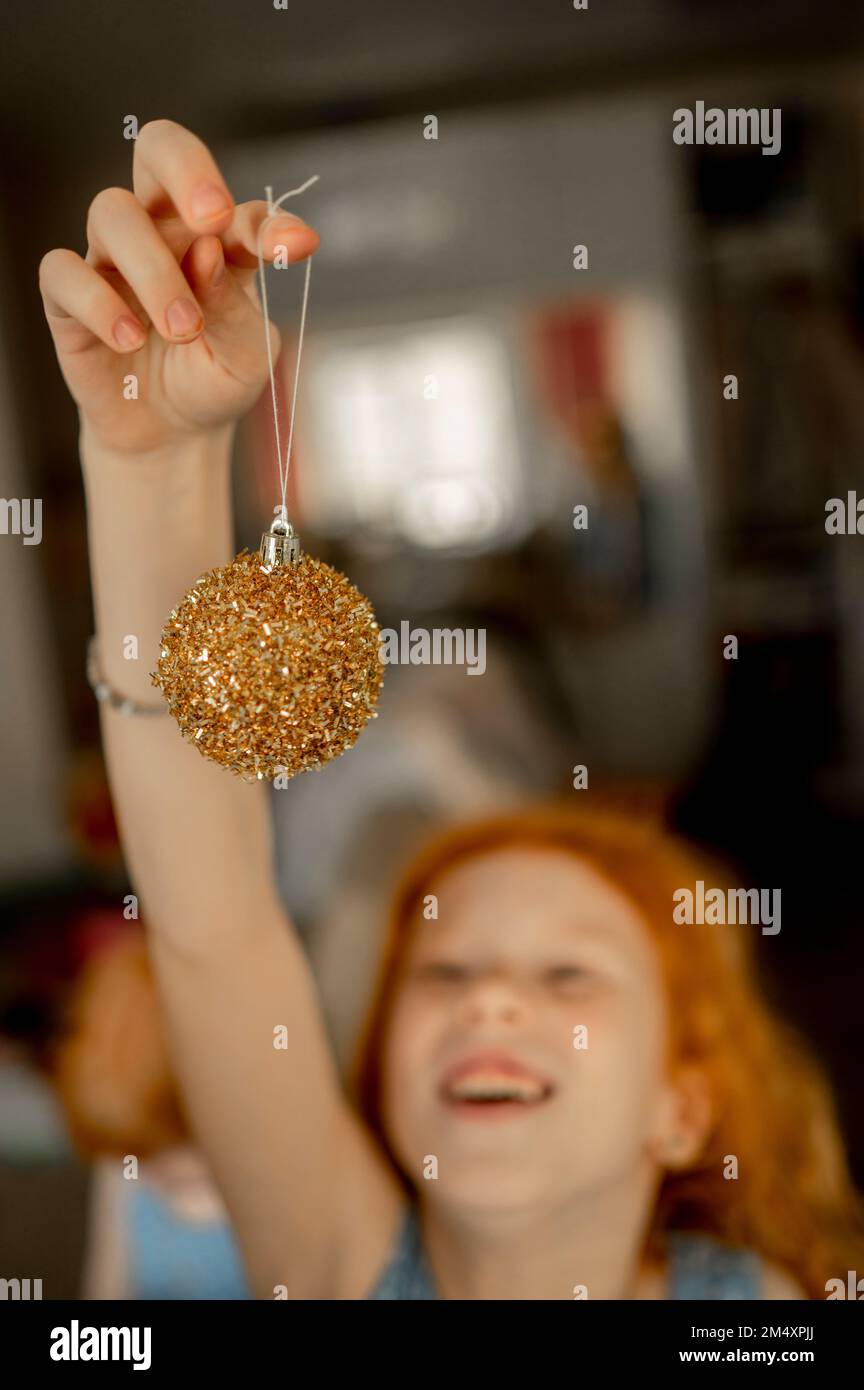 Fille tenant une boule de Noël scintillante à la maison Banque D'Images
