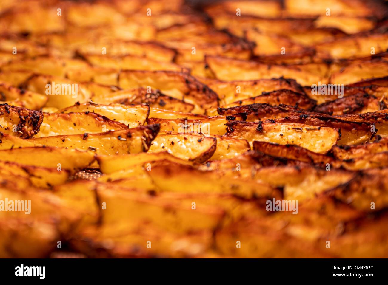 Description: Croustillants, bruns dorés, morceaux de pommes de terre assaisonnés de paprika, ail, sel, poivre, romarin, basilic sur plateau dans le four photographié fr Banque D'Images
