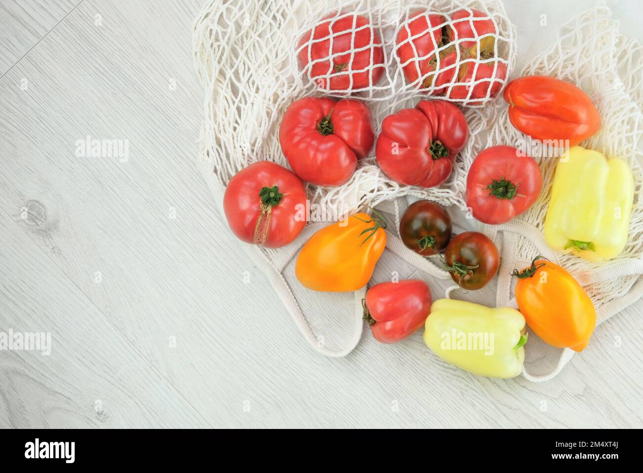 Différentes tomates et poivrons agricoles sur fond de bois blanc. Légumes en sachet de coton. Vue de dessus. Copier l'espace. Banque D'Images