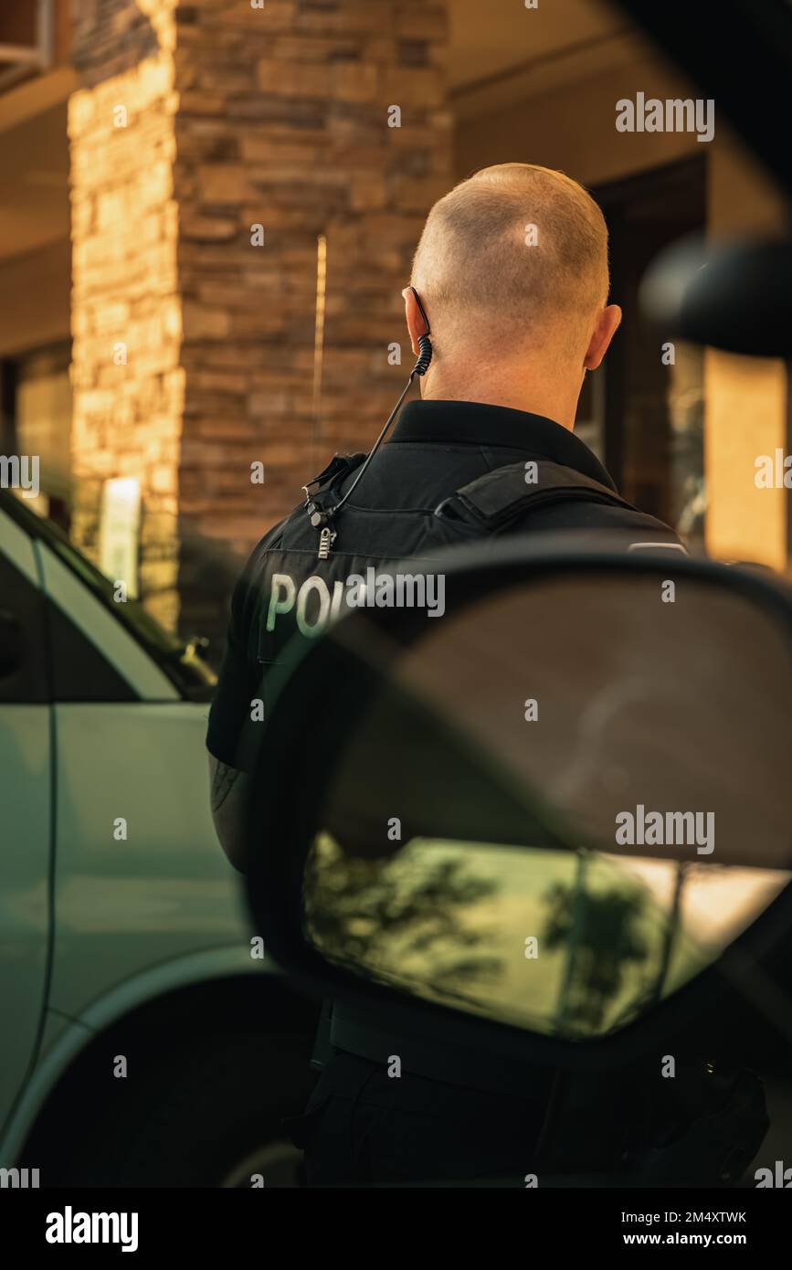 Image verticale de l'officier de police blanc de race blanche debout à l'extérieur du véhicule de la cdp, vu de l'intérieur de la voiture de patrouille. Officier regardant loin de venu Banque D'Images