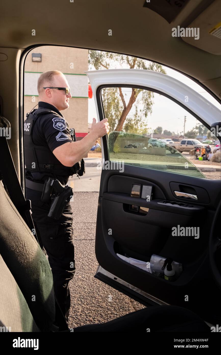 Un policier blanc de sexe masculin sort du véhicule pour enquêter sur une situation dans une ville pendant un après-midi chaud. Banque D'Images