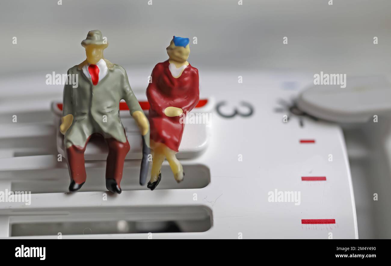 Figures de vieux couple retraité assis chaleureusement habillé sur un thermostat de chauffage à des températures froides sur clip de sauvegarde Banque D'Images