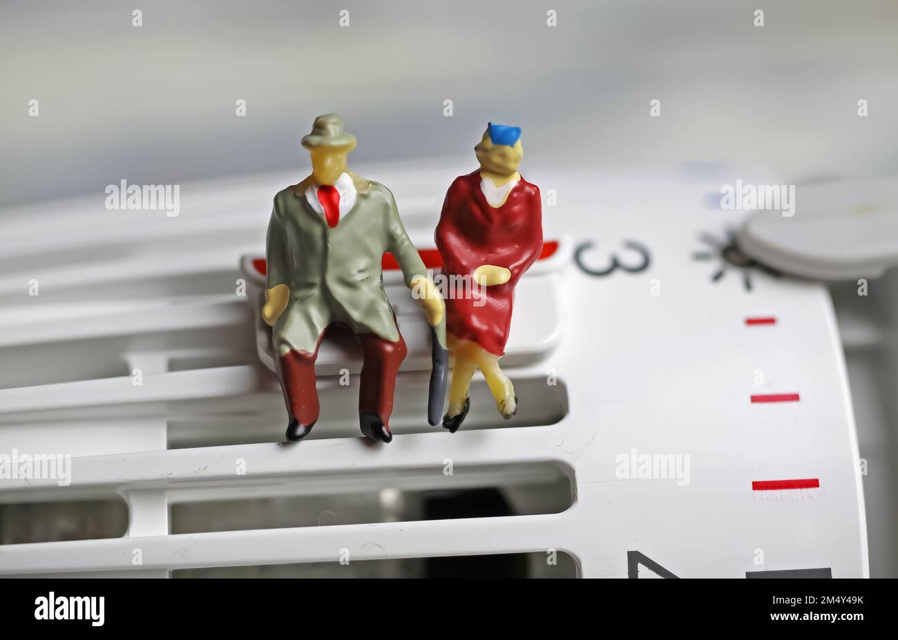 Figures de vieux couple retraité assis chaleureusement habillé sur un thermostat de chauffage à des températures froides sur clip de sauvegarde Banque D'Images