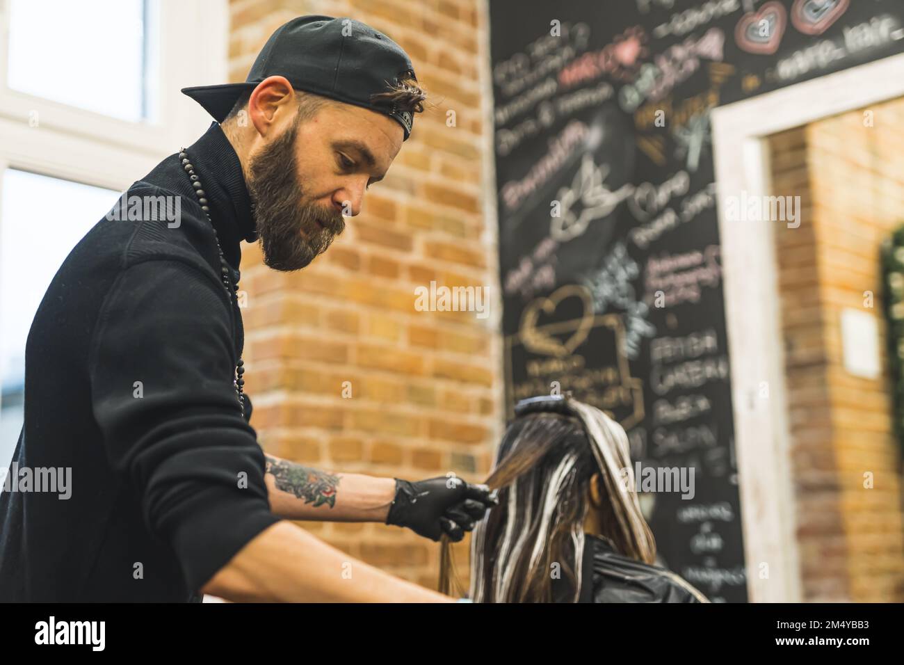 Coiffeur professionnel au travail. Homme de race blanche, adulte moyen, vêtu de tout le noir colorant les cheveux de son client. Portrait d'intérieur de gros plan moyen. Photo de haute qualité Banque D'Images