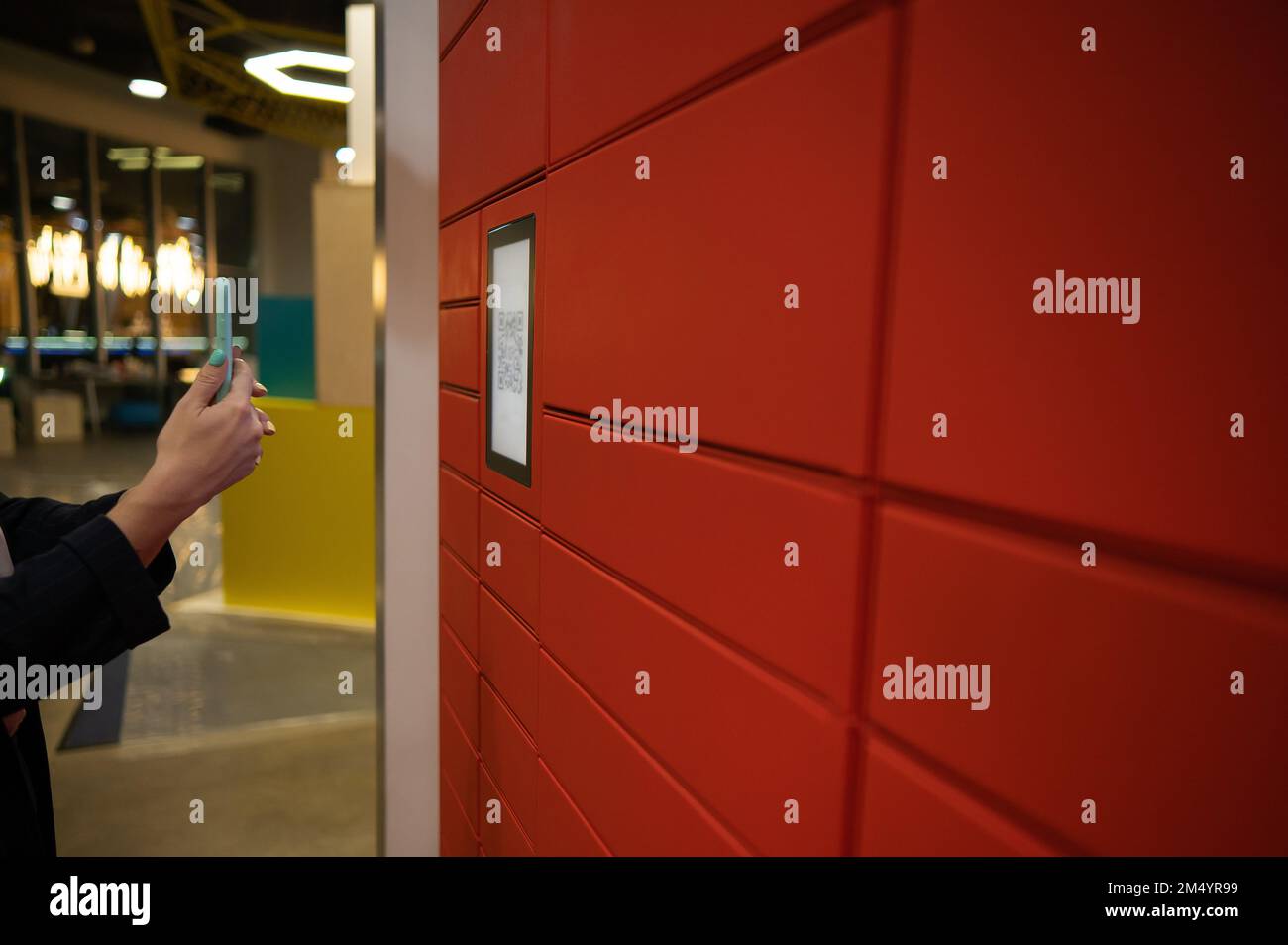 Une femme lit un code rouge pour ramasser un colis à une machine à colis. Boîte postale automatisée. Banque D'Images Une femme lit un code rouge pour ramasser un colis à une machine à colis. Boîte postale automatisée. Banque D'Images