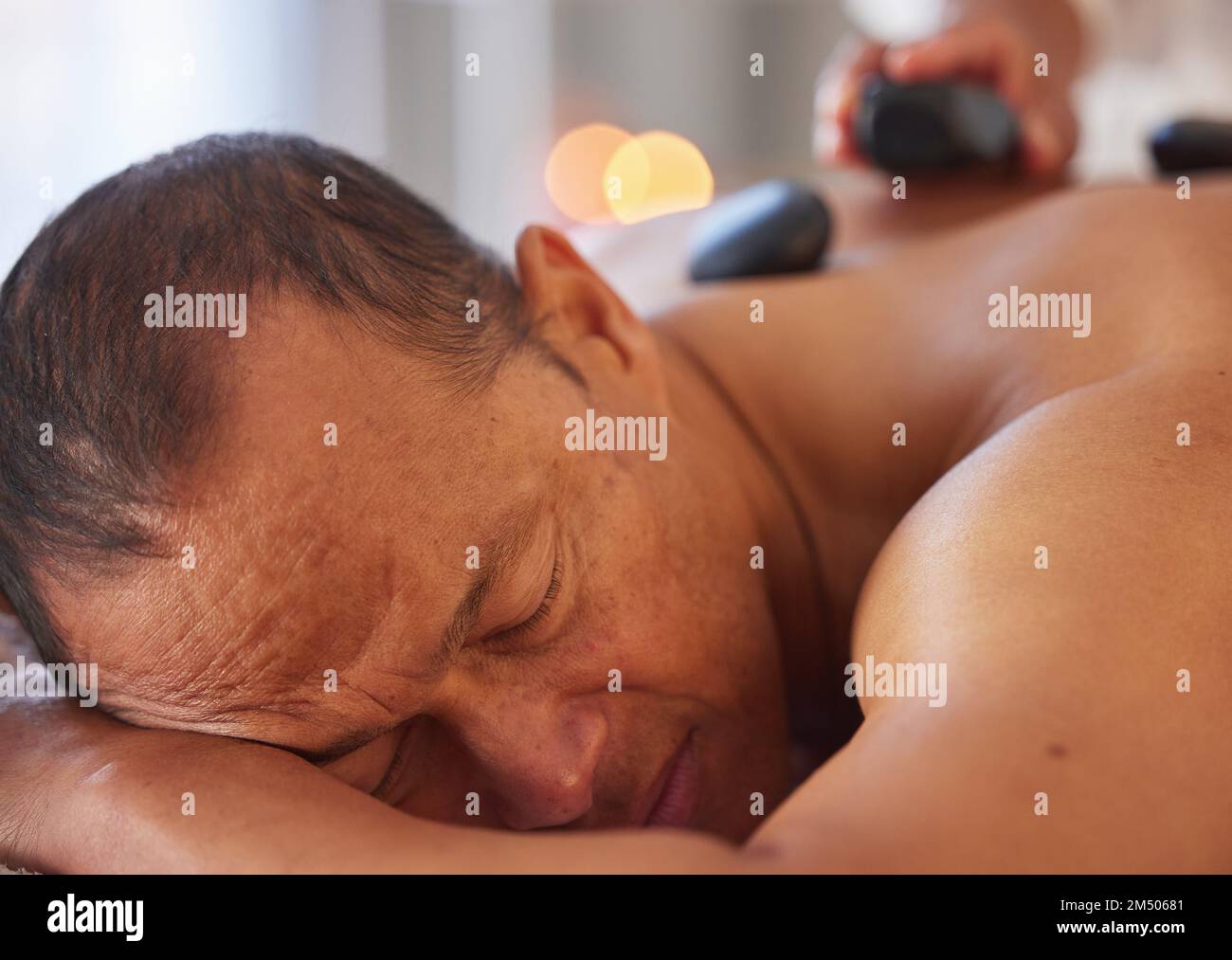 Spa, massage homme et pierre pour se détendre, bien-être et santé pour les soins du corps, la paix et les soins holistiques. Homme, homme et allongé sur une table dans un complexe de luxe Banque D'Images