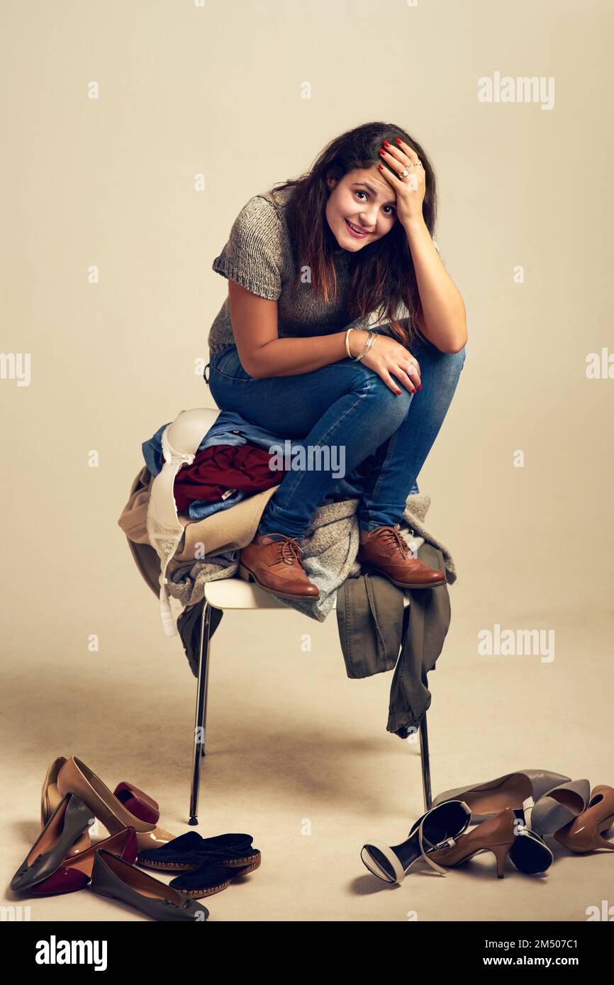 Essayer de trouver la tenue parfaite. La lutte est réelle. Studio photo d'une jeune femme essayant de choisir une tenue d'un tas de vêtements contre un Banque D'Images