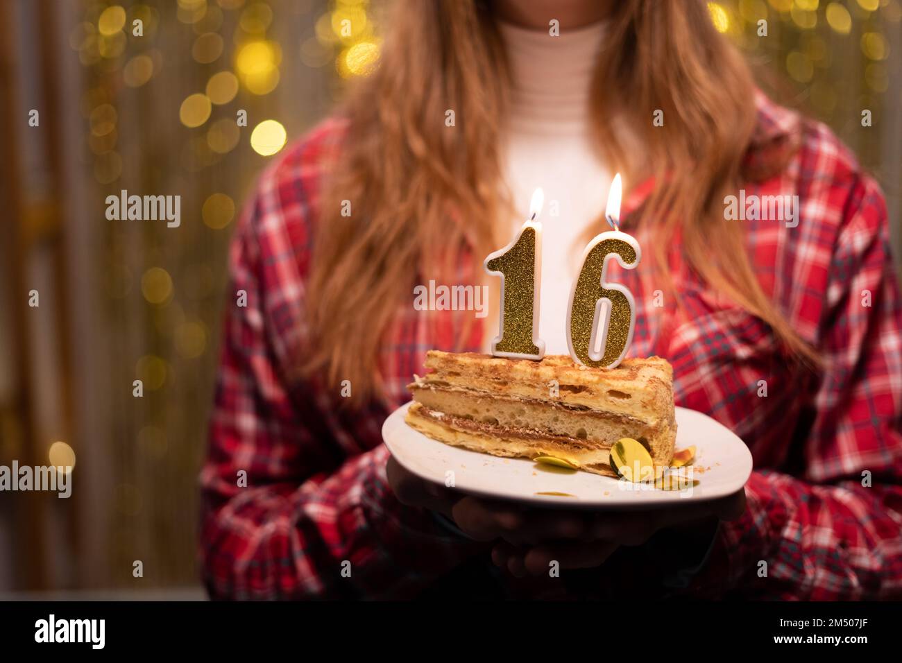 Jeune femme tenant une assiette avec un savoureux gâteau d'anniversaire avec 16 numéros de bougie contre des lumières défocused. Copier l'espace Banque D'Images