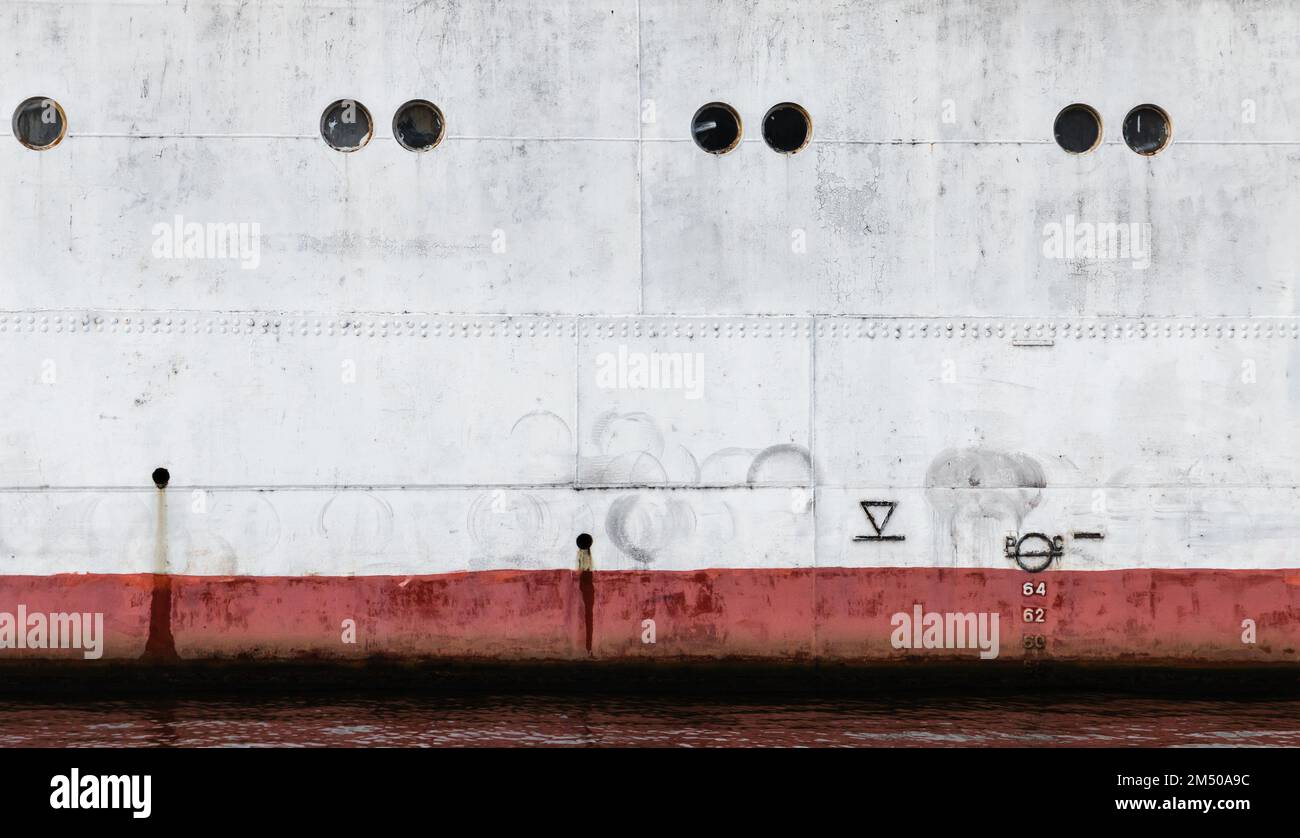 Coque de bateau blanc vintage avec ligne d'eau et hublots rouges, texture de fond industrielle Banque D'Images