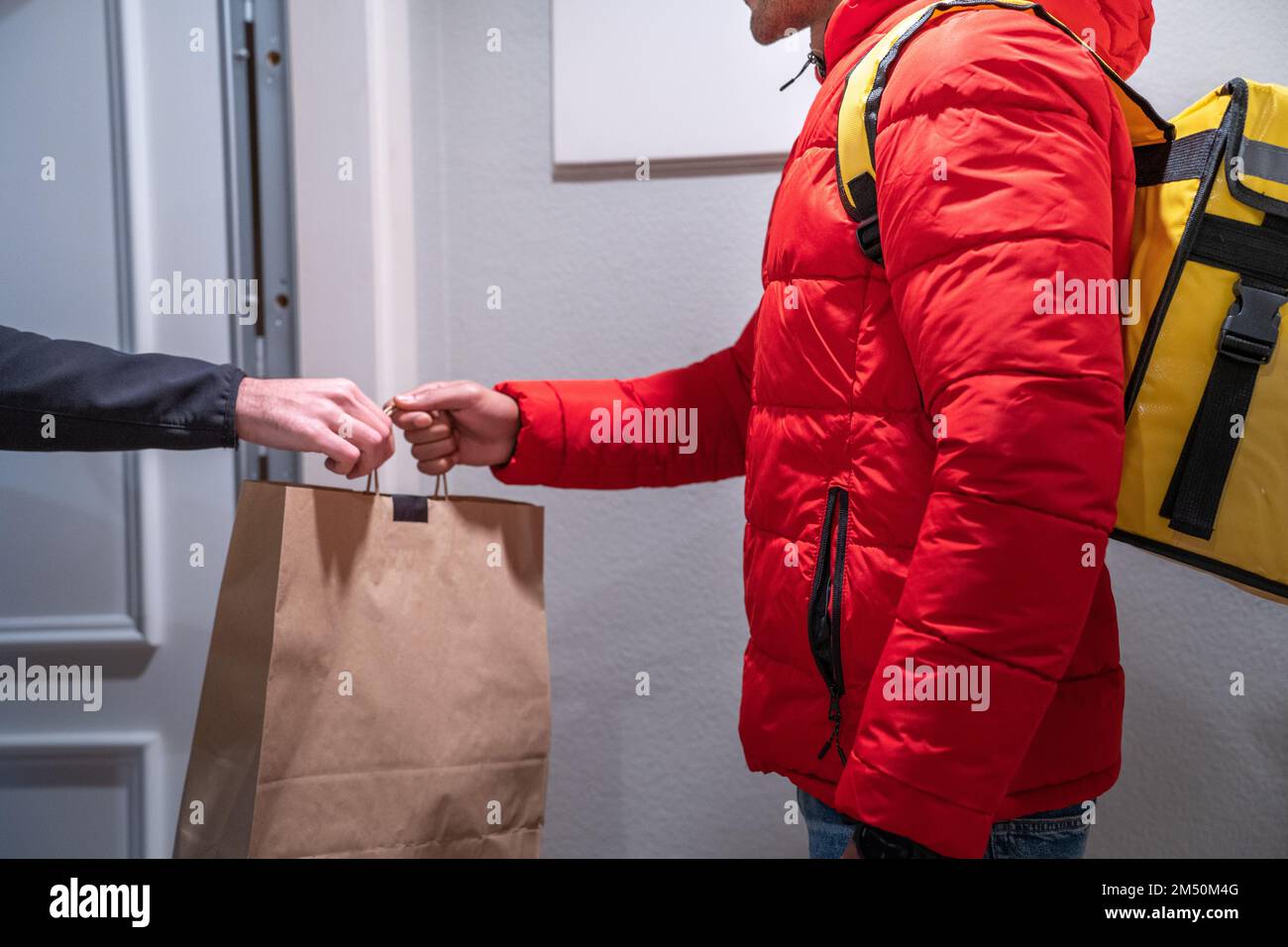 Un livreur d'aliments méconnaissable livre un sac d'aliments à un client qui a commandé en ligne. Banque D'Images