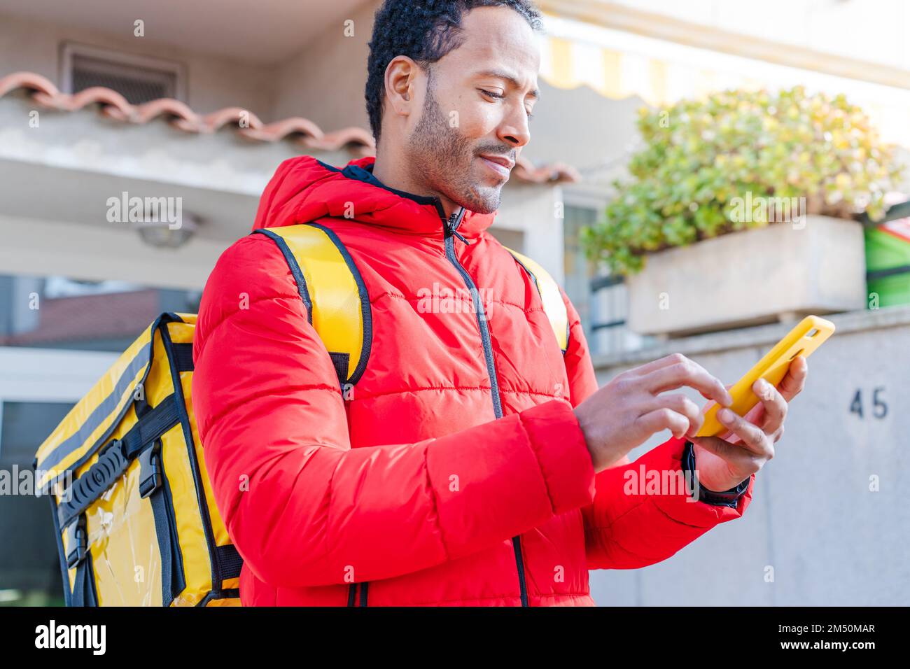 Messager avec sac à dos jaune recherche d'adresse avec téléphone mobile. Concept de livraison de nourriture Banque D'Images