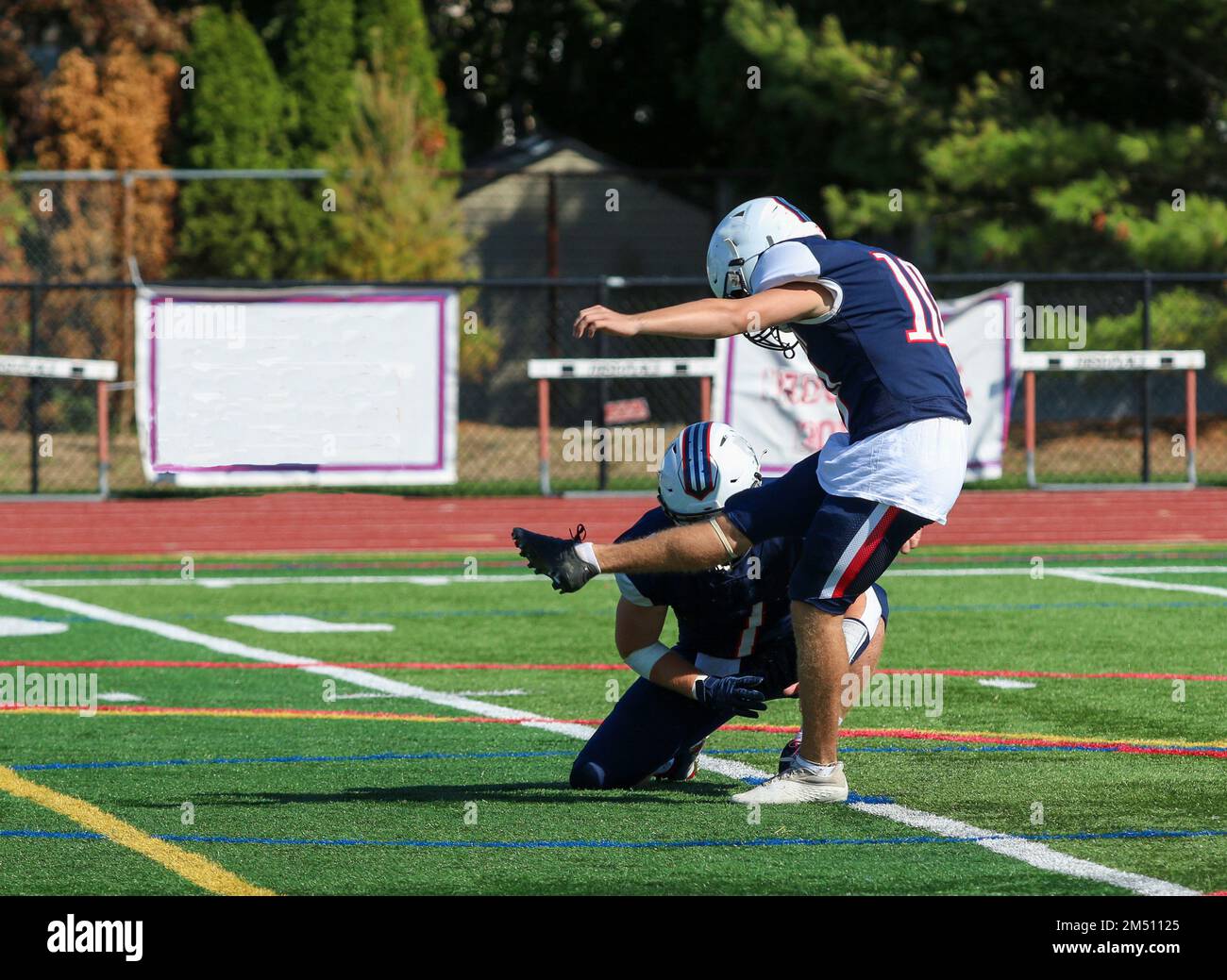 Vue latérale d'un joueur de football d'école secondaire qui donne un coup de pied à un but de terrain pendant un match. Banque D'Images
