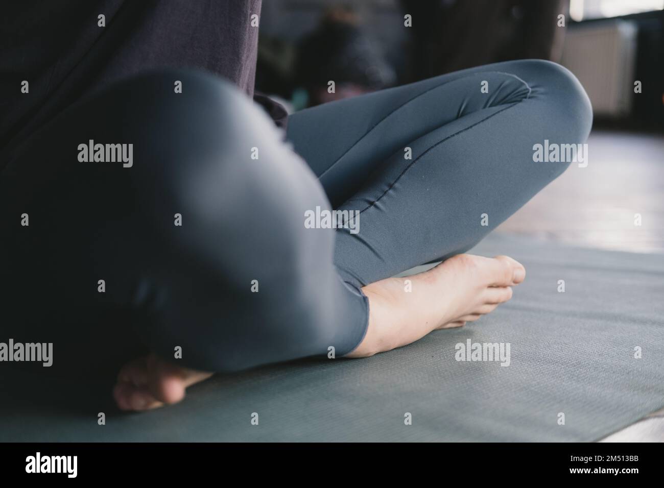 Photo en gros plan des jambes d'une femelle yogi méditant pieds nus et portant des leggings en posture facile (sukhasana) sur un tapis de yoga sur le sol Banque D'Images