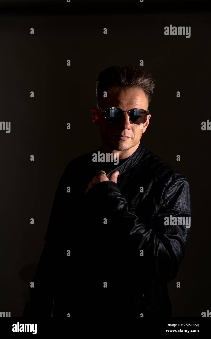 Portrait d'un homme beau. Sexy homme élégant habillé dans une veste en cuir et des lunettes de soleil. Mode hipster mâle isolé sur fond gris en studio Banque D'Images