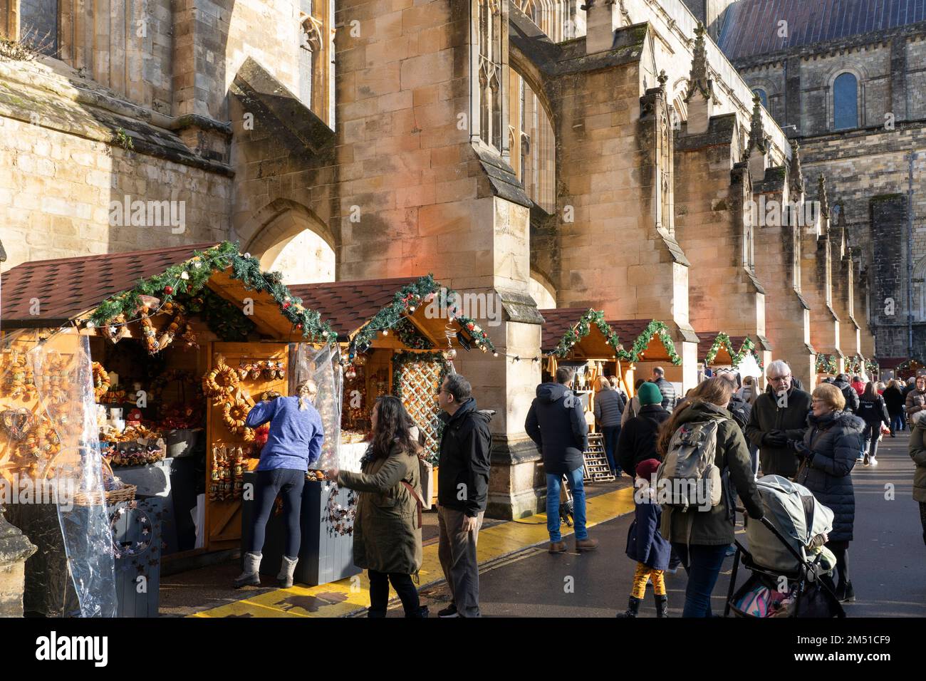 Les acheteurs de Noël au marché de Noël de Winchester avec des étals entre les contreforts volants en pierre de la cathédrale gothique de Winchester, Angleterre, Royaume-Uni Banque D'Images