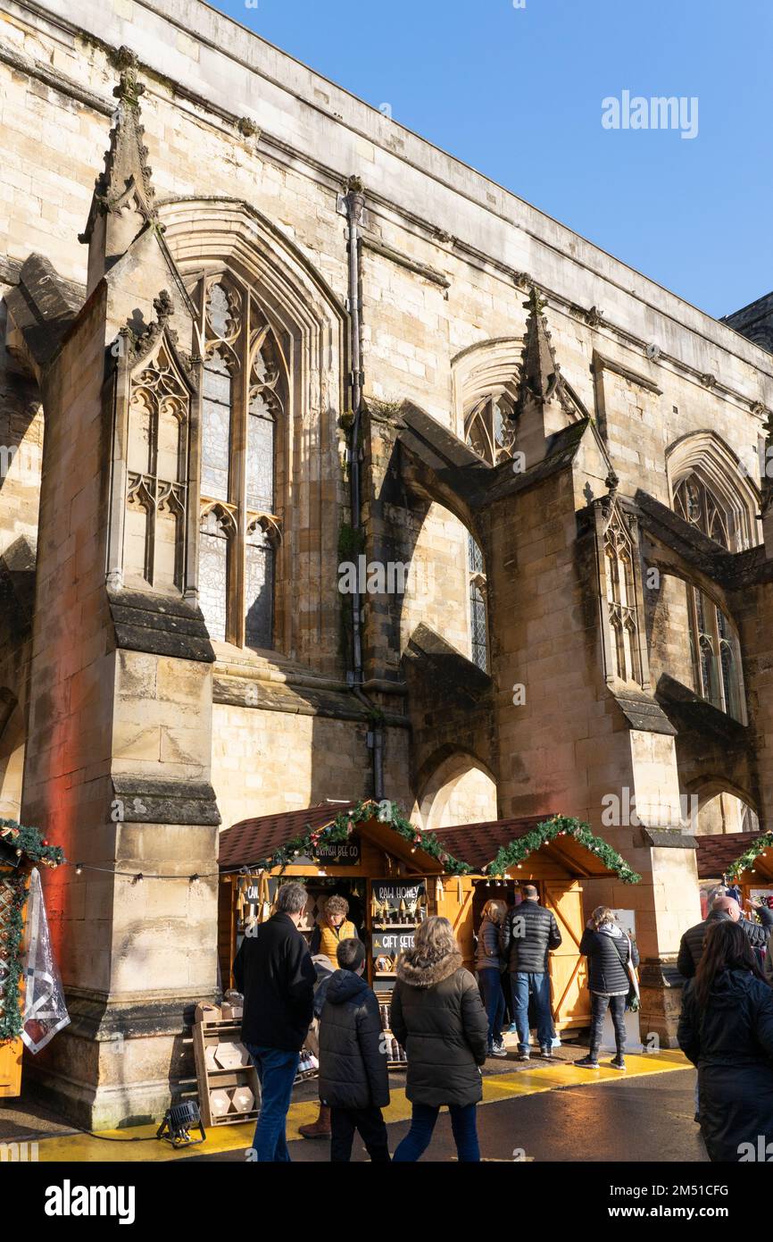 Les acheteurs de Noël au marché de Noël de Winchester avec des étals entre les contreforts volants en pierre de la cathédrale gothique de Winchester, Angleterre, Royaume-Uni Banque D'Images