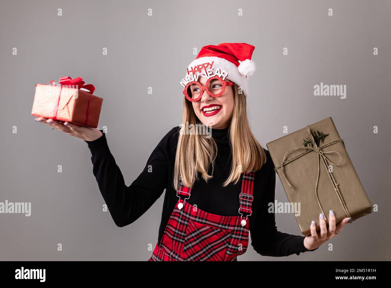 Belle, jeune, blonde fille avec chapeau de père Noël et prop-verres, tenant une boîte cadeau, plus grand et plus petit. Copier l'espace Banque D'Images