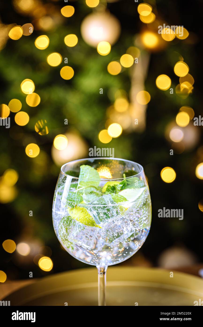 Verre transparent au verre avec glace, et citron vert sur un tableau rustique sombre dans la décoration de Noël avec arbre de Noël et lumières dans le dos flou Banque D'Images