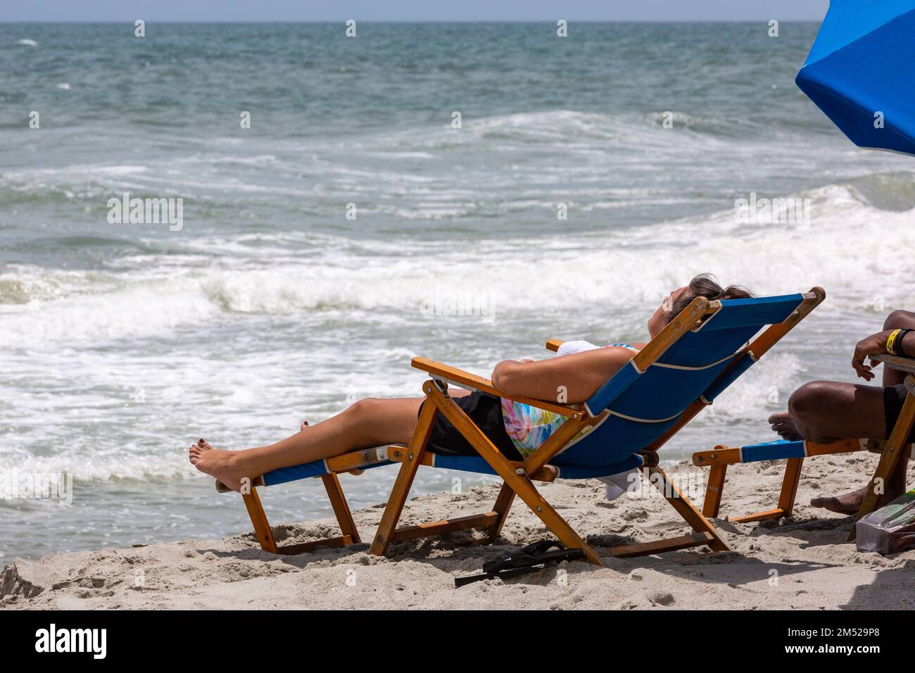 Un bain de soleil se détend dans une chaise de plage bleue sur le sable à Myrtle Beach, Caroline du Sud, États-Unis. Banque D'Images