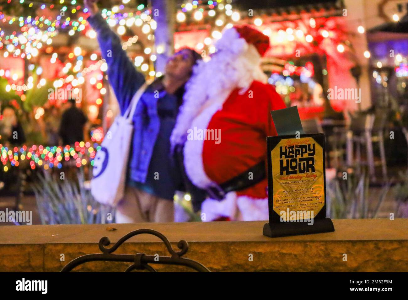 Santa Barbara, Californie, États-Unis 23rd déc. 2022. Drew Wakefield habille comme le Père Noël et est accroché devant le restaurant Pascucci, sur la rue State au centre-ville de Santa Barbara, posant pour un Selfie avec un résident local, derrière un panneau « Happy Hour » le week-end de Noël. (Image de crédit : © Amy Katz/ZUMA Press Wire) Banque D'Images