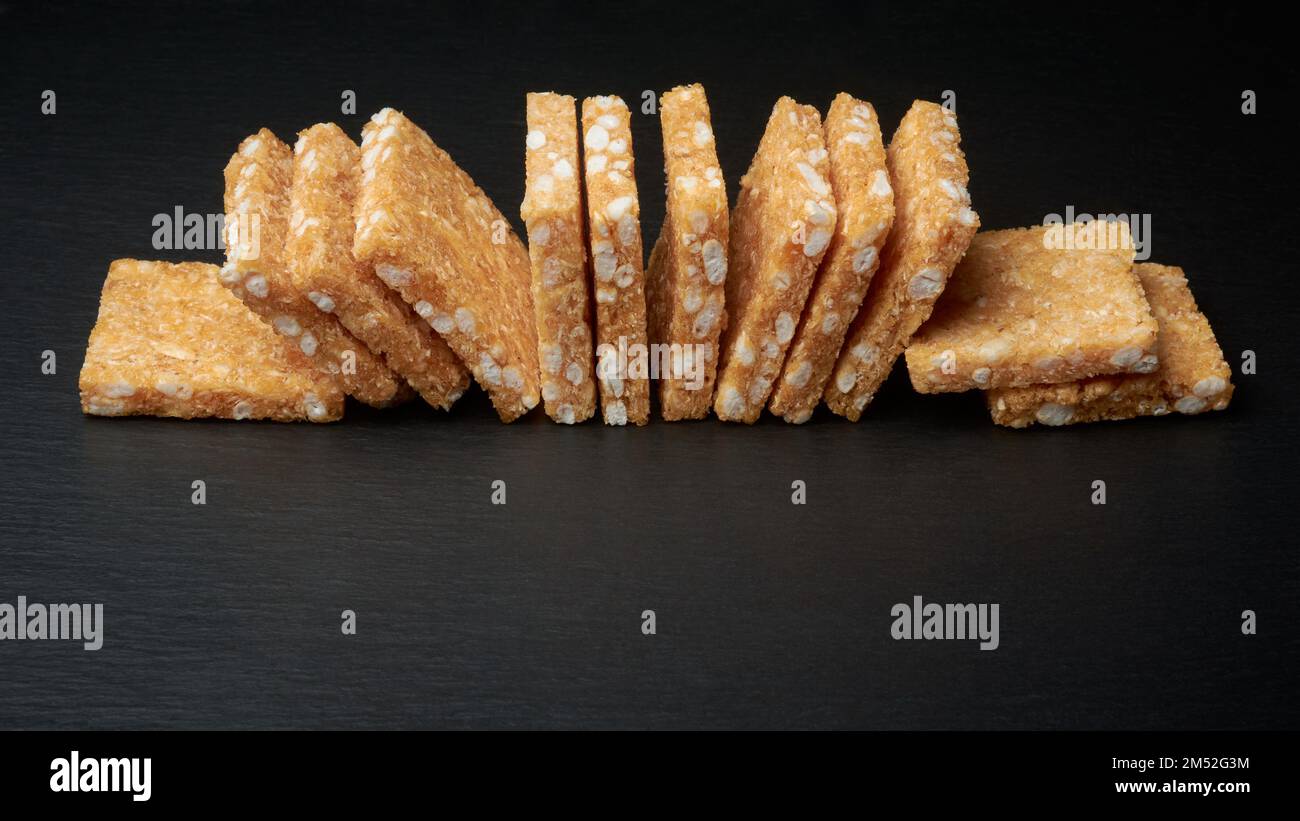 biscuits à la noix de coco, biscuits faits maison en forme de carré croustillant texturé isolés sur la surface de table noire, mise au point sélective avec espace de copie Banque D'Images