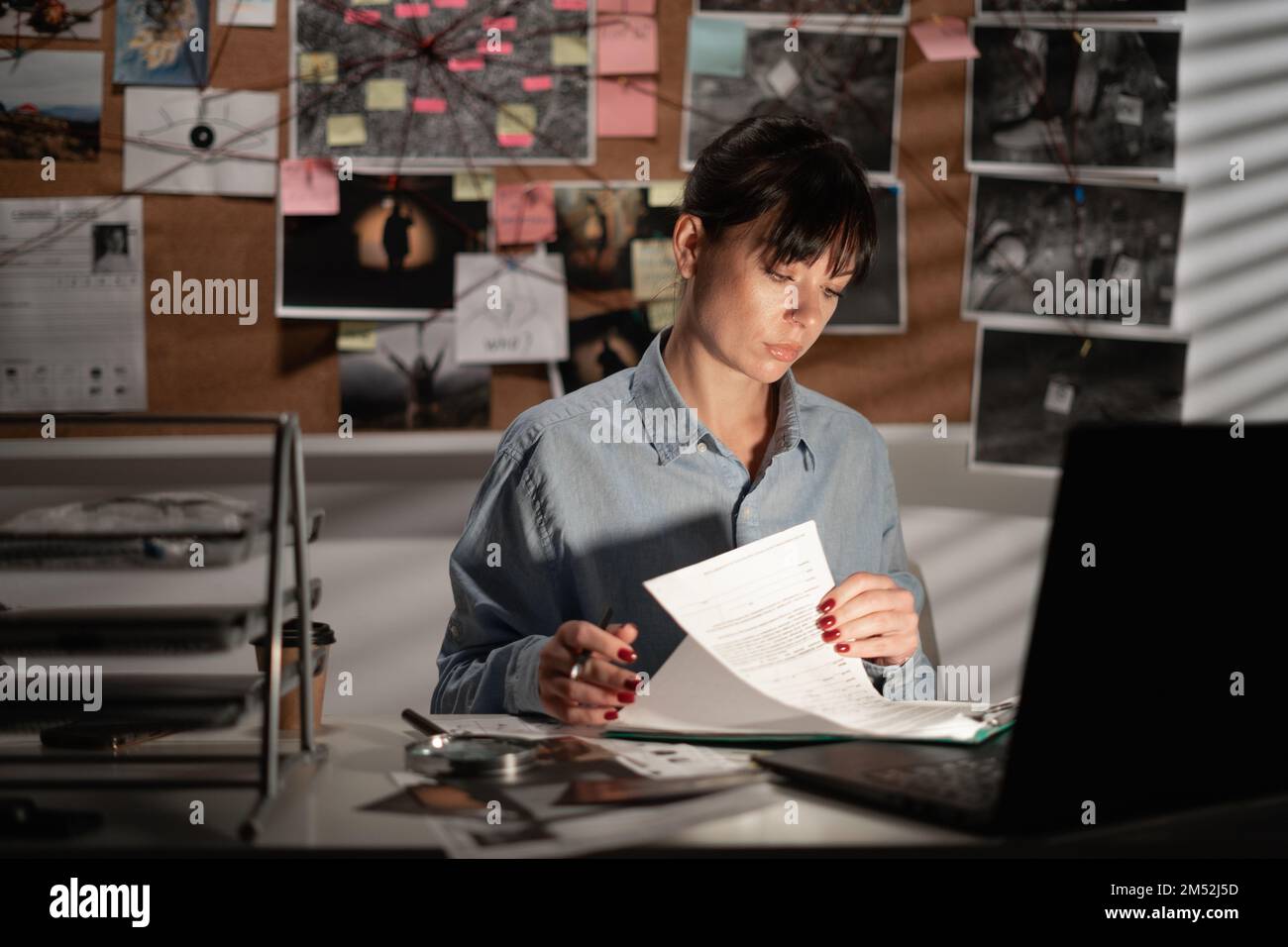 Une femme détective traite les preuves au bureau en utilisant un ordinateur portable la nuit. Copier l'espace Banque D'Images