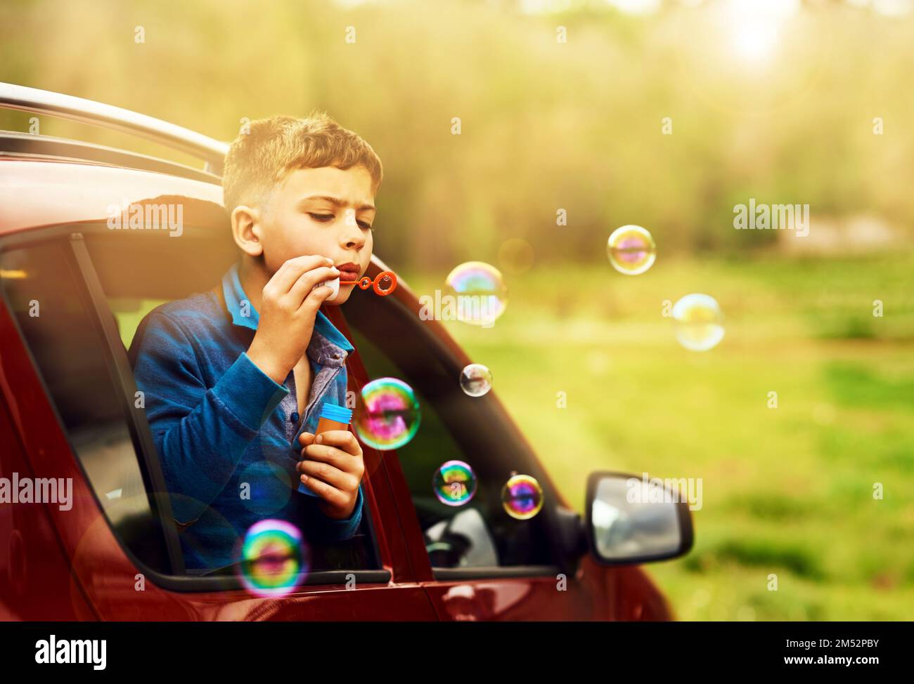 Les bulles parfaites nécessitent une mise au point et une technique. un petit garçon amusant qui souffle des bulles tout en s'inclinant hors de la fenêtre d'une voiture. Banque D'Images