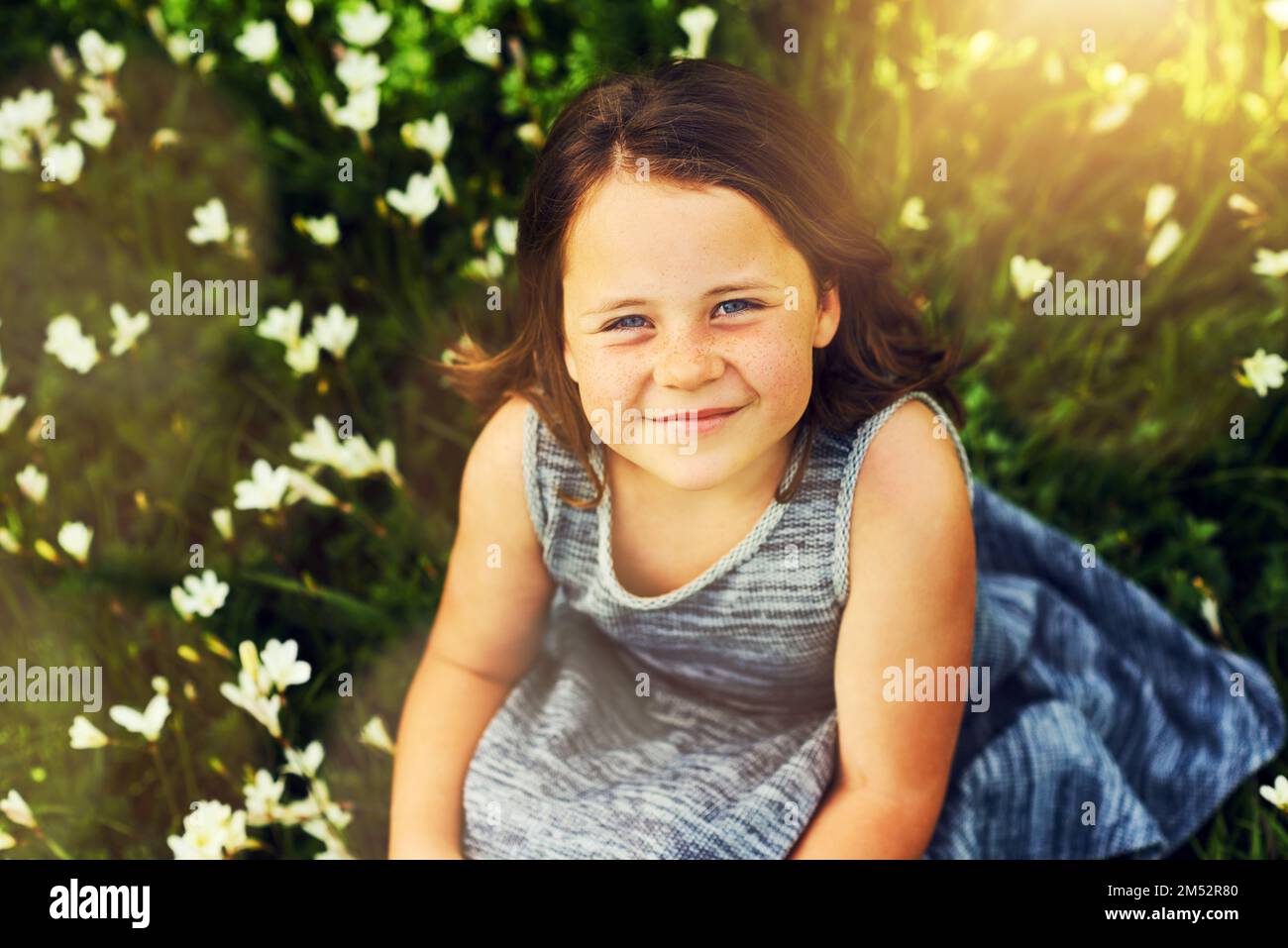 J'appartient entre les fleurs. Portrait d'une petite fille douce assise dans un champ de fleurs sauvages. Banque D'Images