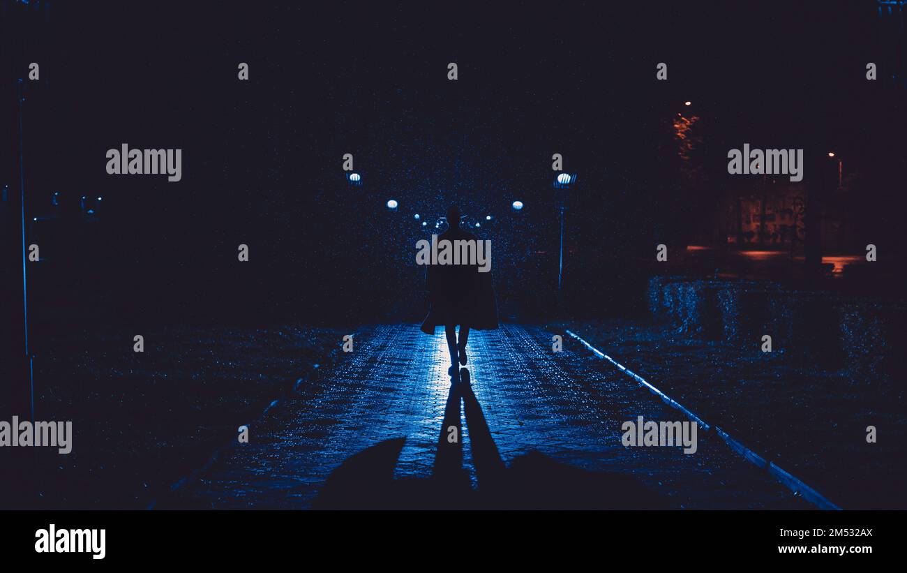 détective masculin dans un chapeau et imperméable la nuit dans une ville pluvieuse dans le style de film noir Banque D'Images