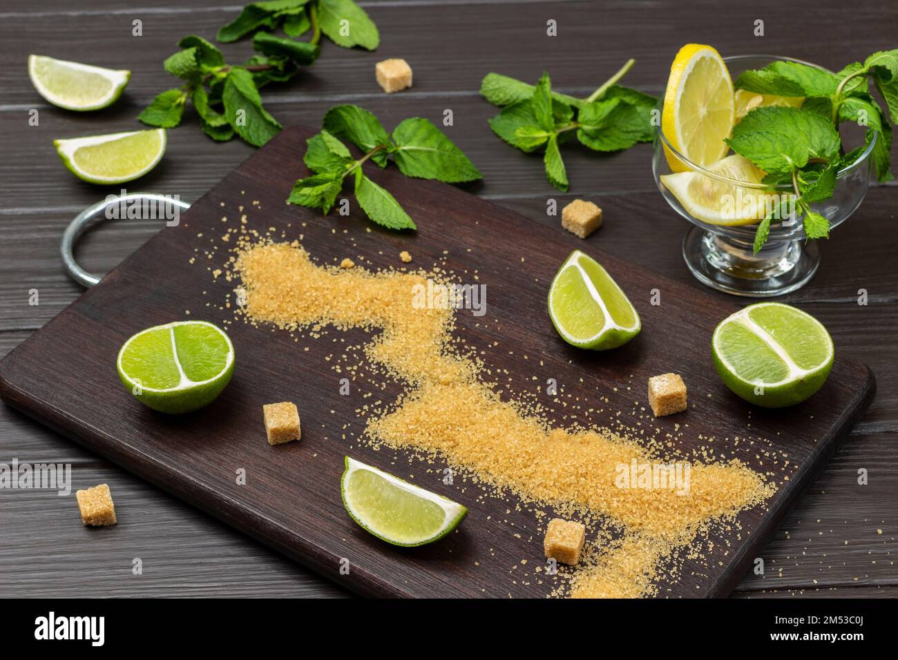 Tranches de sucre brun et de lime à bord. Des branches de menthe sur la table. Citron dans un bol en verre. Vue de dessus. Arrière-plan en bois sombre. Banque D'Images