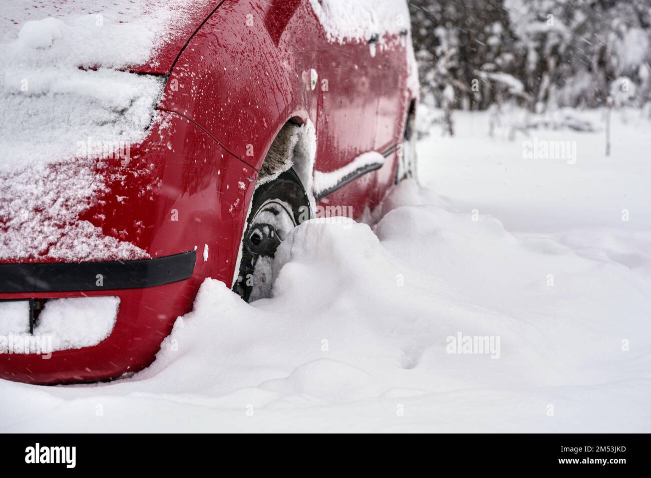 Voiture rouge garée dans une couche épaisse de neige après une tempête de neige intense, détail sur le pneu - seulement une demi-roue visible Banque D'Images
