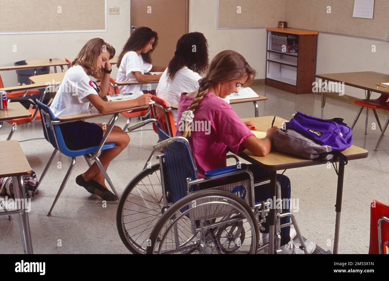 Les adolescentes sont assises à leur bureau dans la salle de classe. Une des filles assis dans un fauteuil roulant Banque D'Images