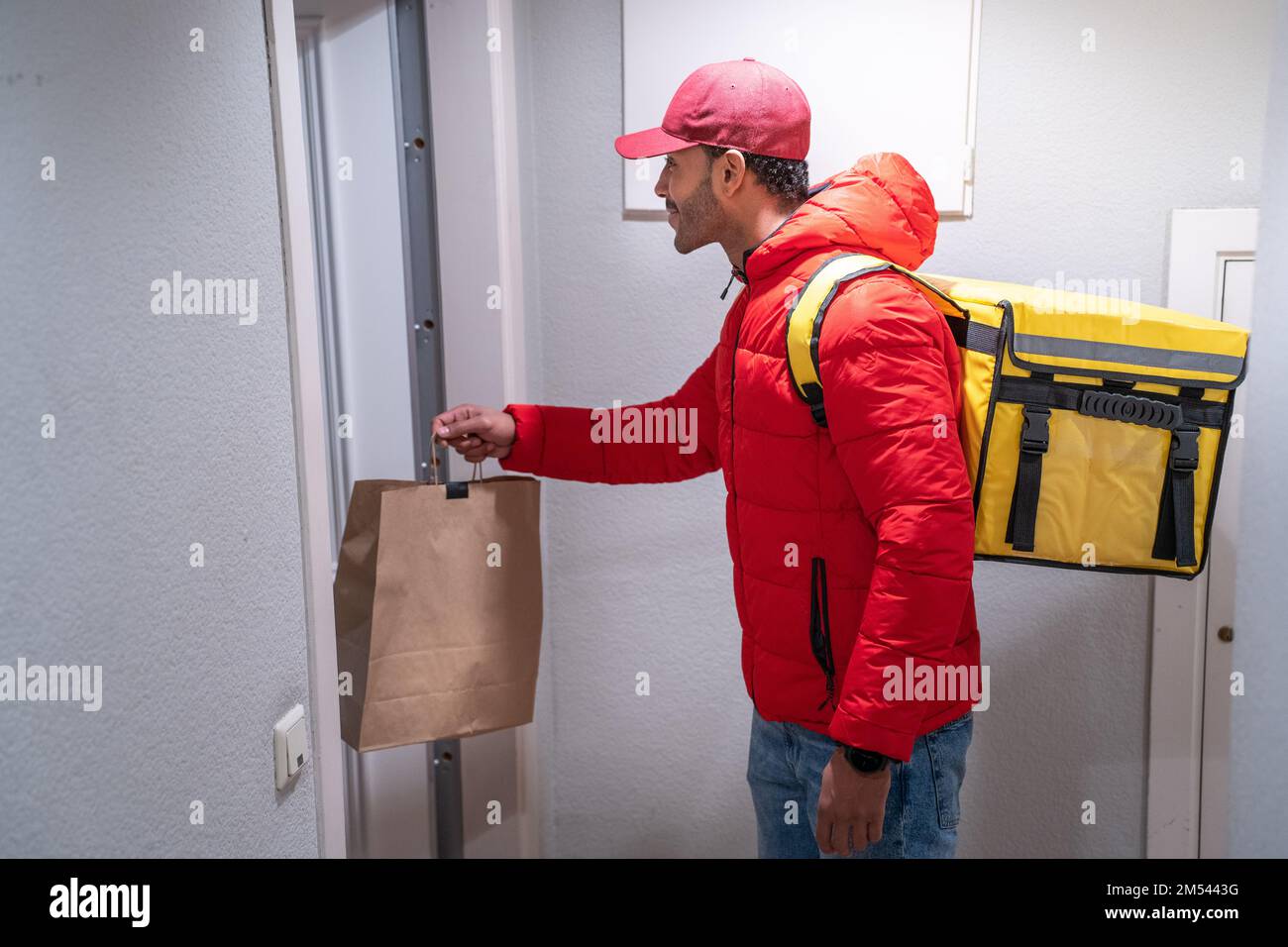 Bon livreur en uniforme rouge avec sac à dos livre un sac de nourriture. Banque D'Images