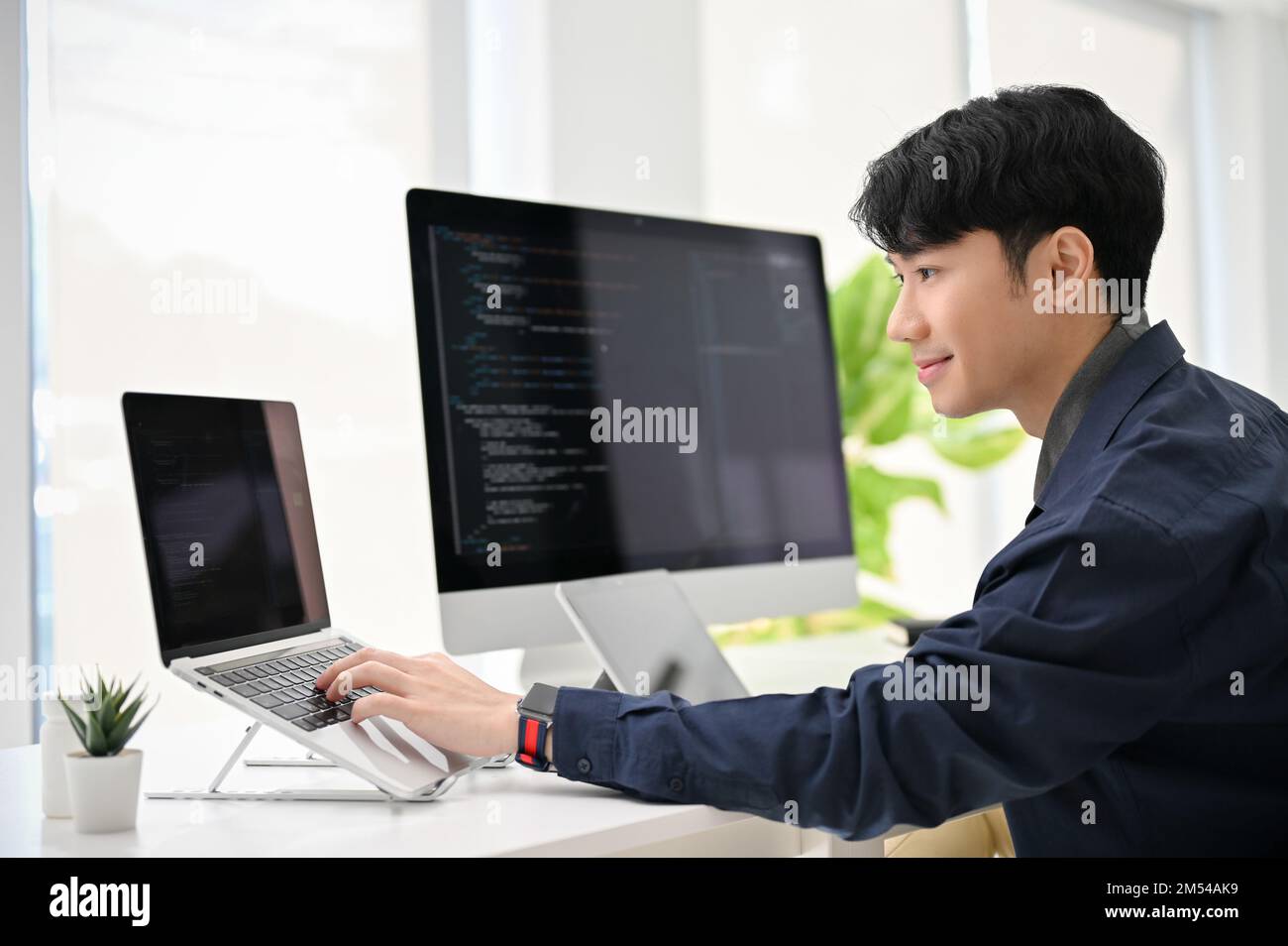 Un jeune programmeur asiatique professionnel et intelligent codant à son bureau, travaillant sur son projet, utilisant un ordinateur portable et un ordinateur. Banque D'Images