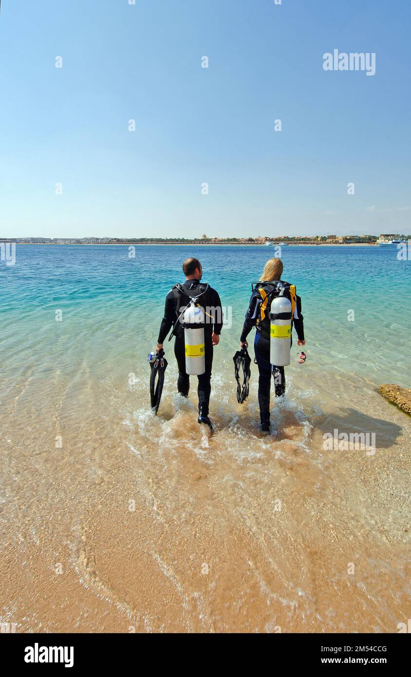 Jeune couple jeune homme et jeune femme marchant avec de l'équipement de plongée sous-marine pour la plongée sous-marine côte à côte sur la plage de la mer Rouge, Makadi Banque D'Images