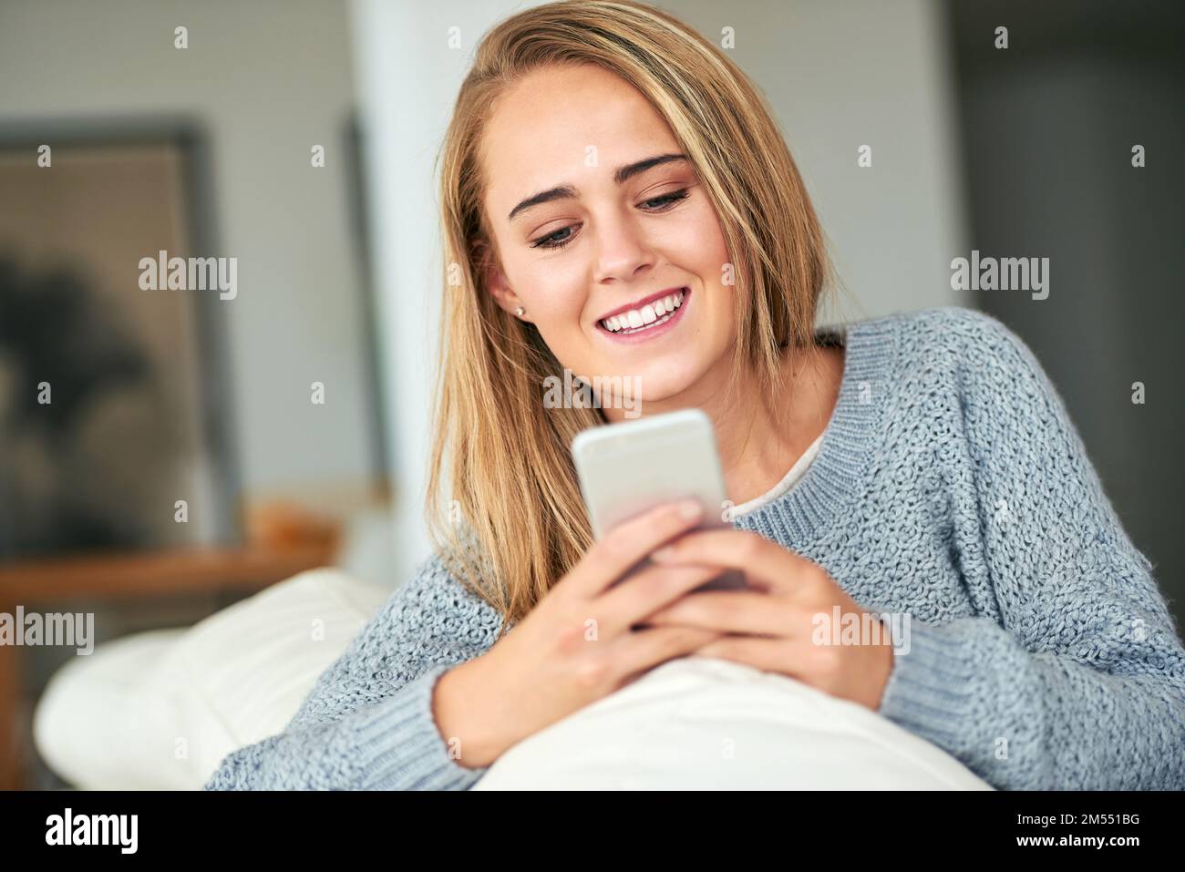 Certains textes ont le pouvoir de faire votre journée. une jeune femme attirante envoyant un message texte tout en se détend à la maison. Banque D'Images
