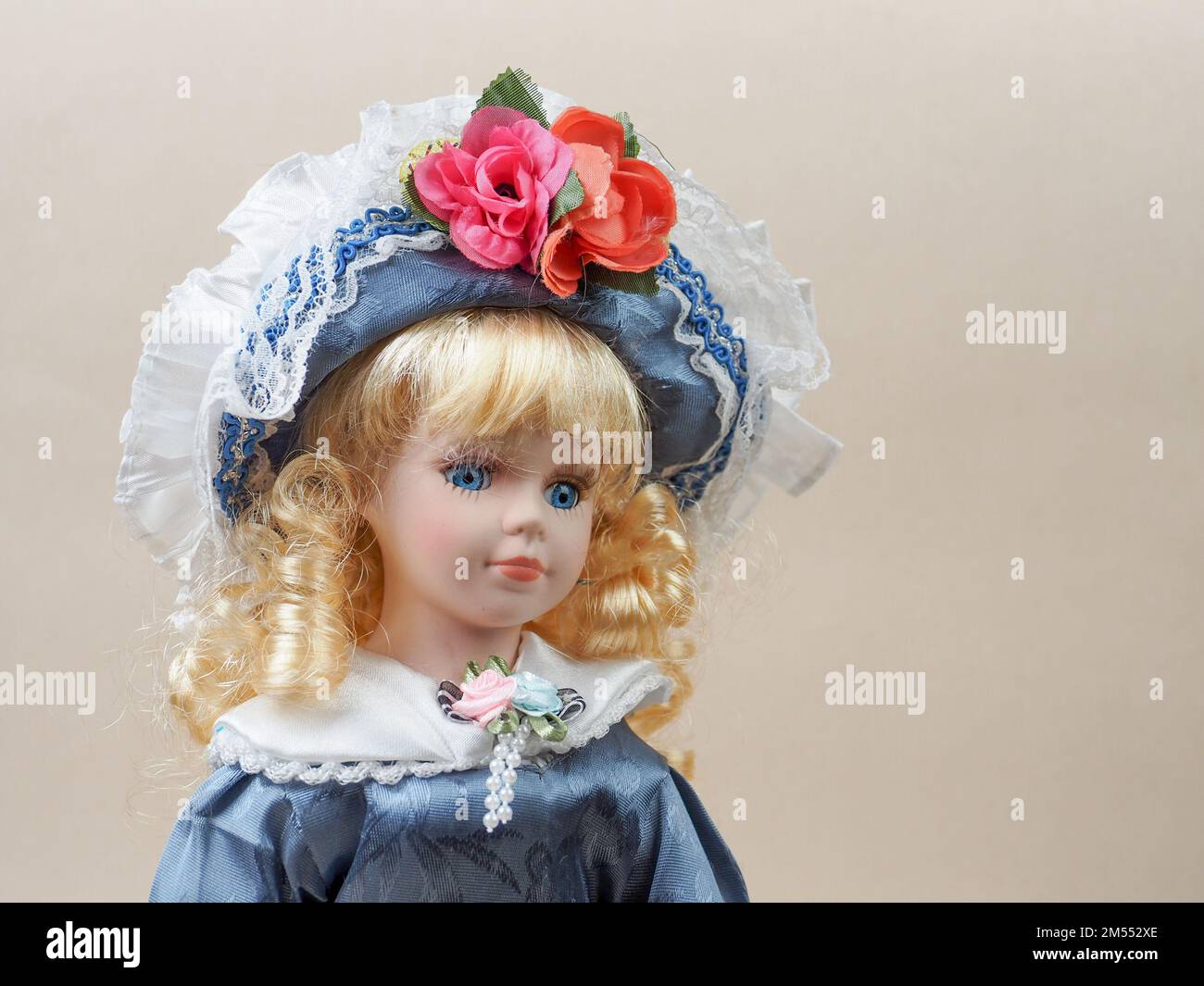 Poupée en porcelaine vintage bébé fille avec des yeux bleus, boucles  blondes, portant un chapeau bleu décoré de fleurs rouges et une robe bleue  en satin. Les poupées en porcelaine étaient populaires