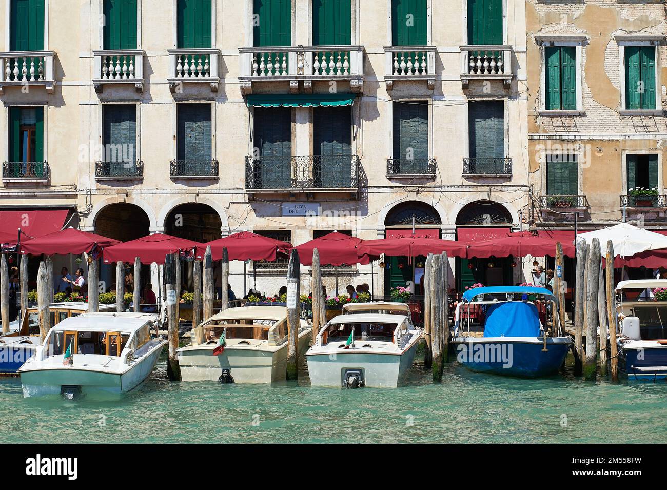 Vue sur le quartier des restaurants du Rialto avec des auvents rouges et des bateaux amarrés sur les poteaux en bois typiques, Venise, Italie Banque D'Images