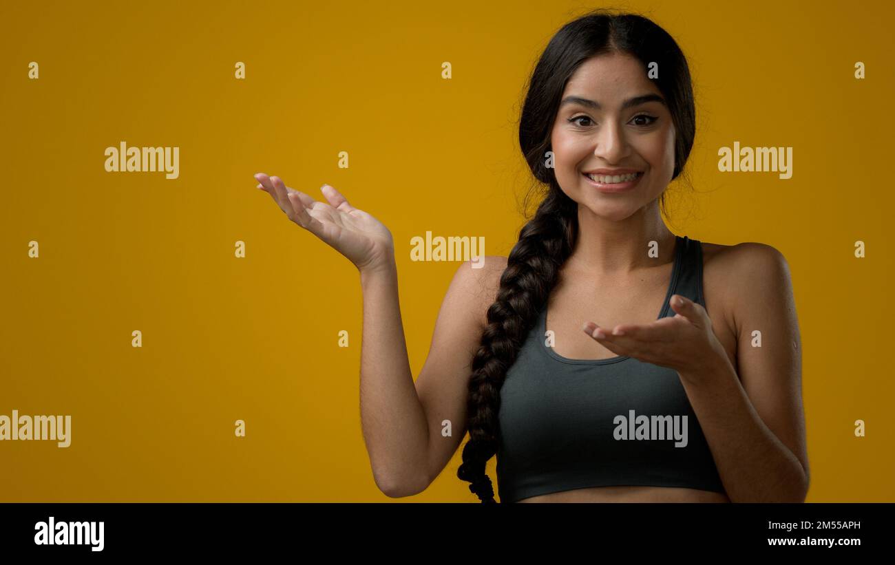 Femme indienne satisfaite fille femelle regardant l'appareil photo dans le studio fond jaune pointant sur le côté vide espace de copie publicité étonnement étonnant Banque D'Images