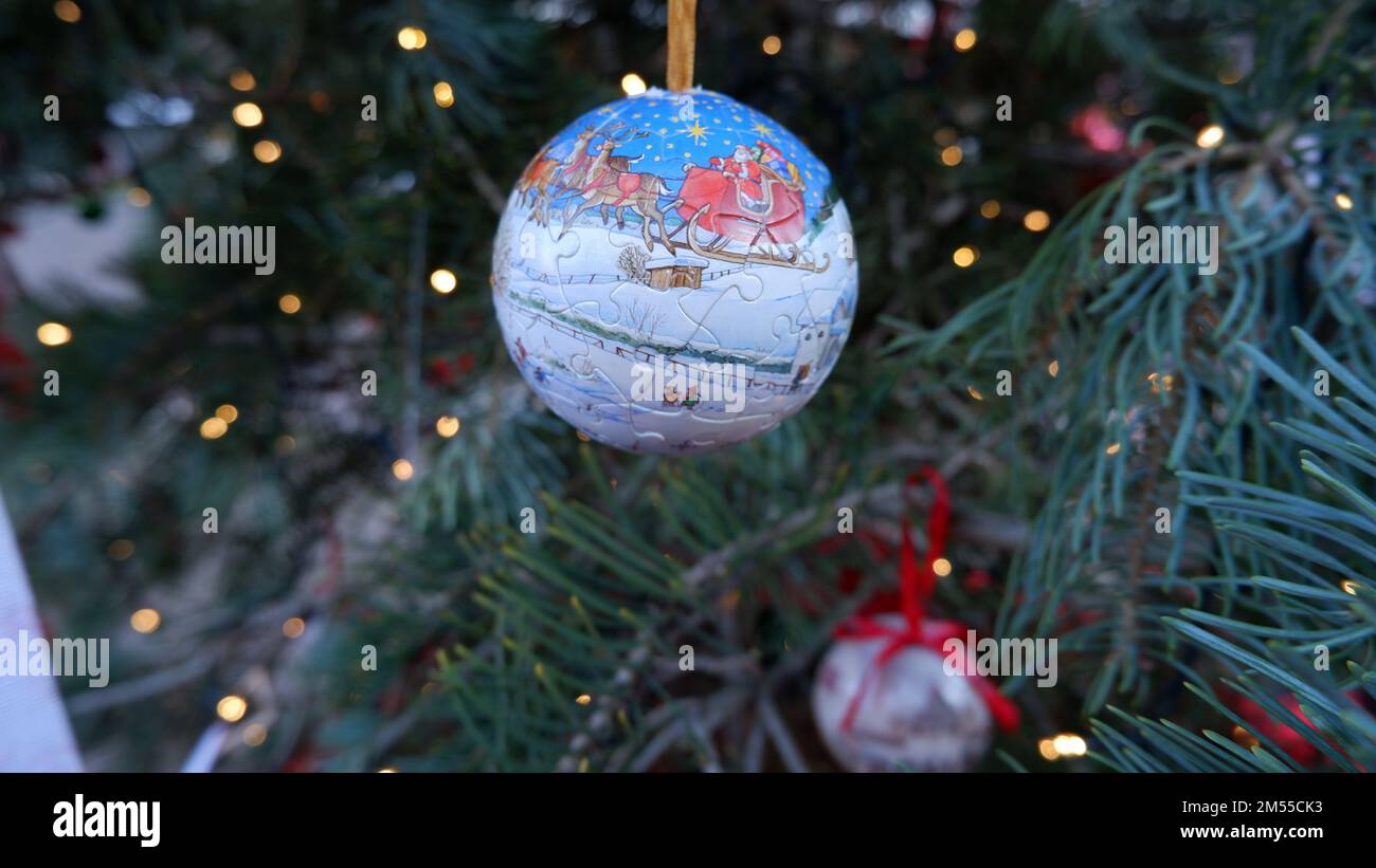 Une boule de puzzle avec le père Noël ou Saint Nicholas dans sa voiture avec le cerf sur la neige accrochée d'un pin, foyer sélectif et gros plan. Banque D'Images