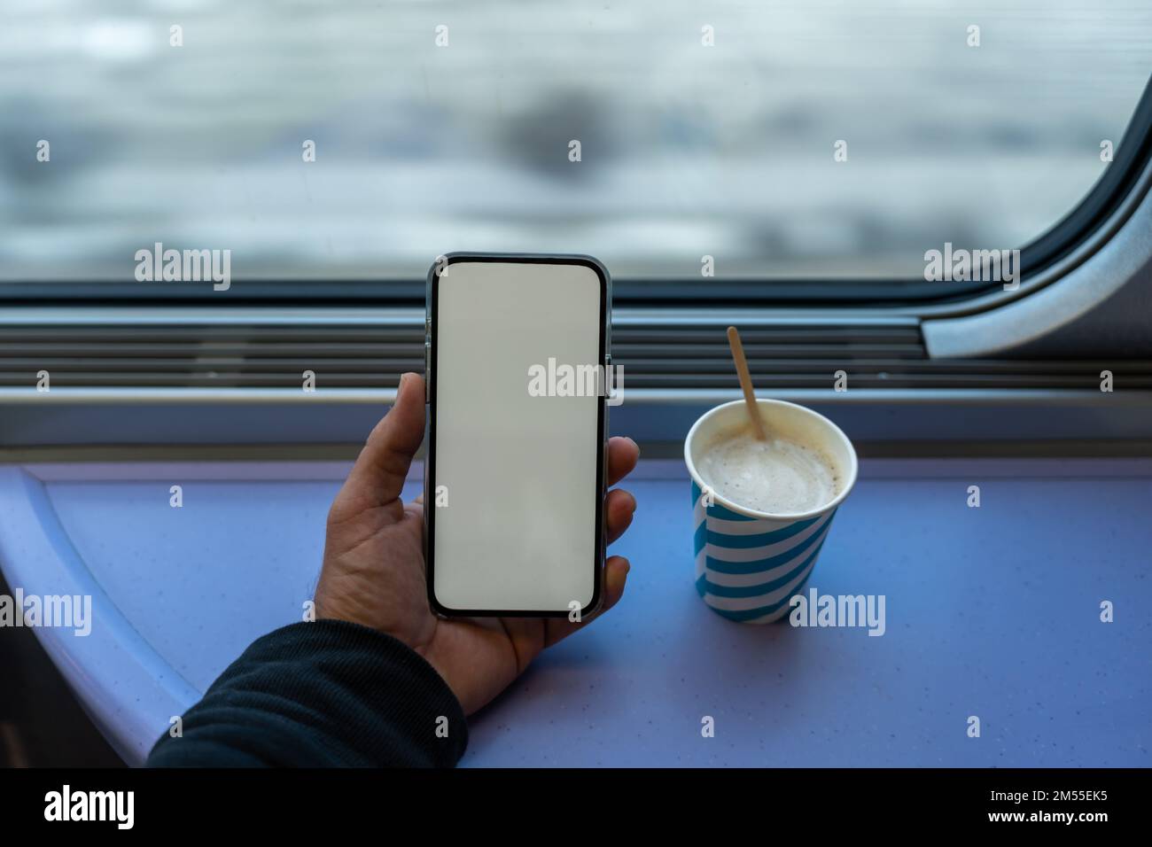 Depuis le dessus, les passagers anonymes naviguent sur un smartphone avec un écran vide près d'une tasse de café contre la fenêtre du train pendant le voyage Banque D'Images
