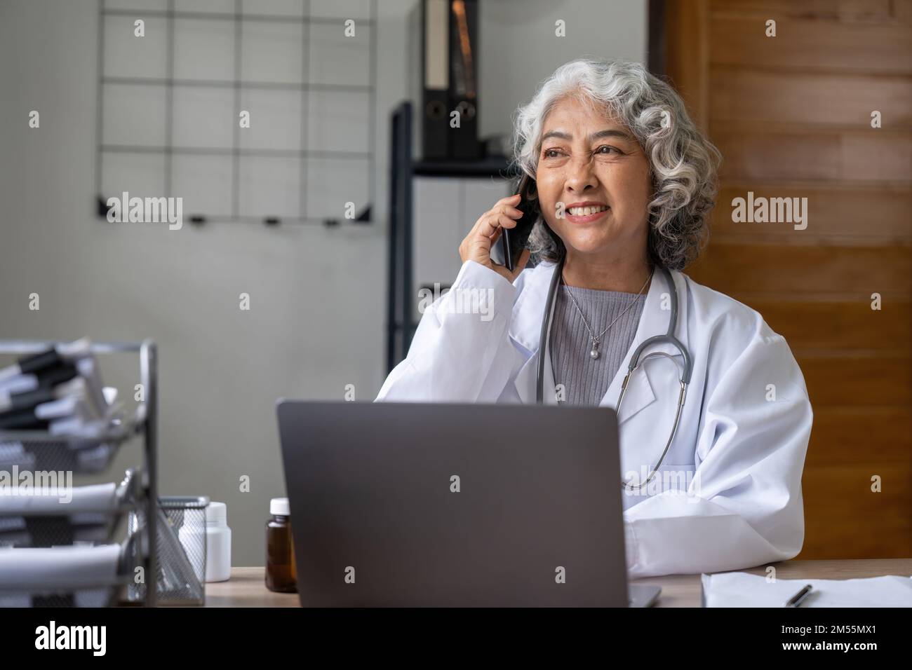 Médecin asiatique senior utilisant un téléphone portable parlant alors qu'elle est assise dans le bureau de l'hôpital. femme heureuse médecin travailleur ayant une conversation joyeuse avec Banque D'Images