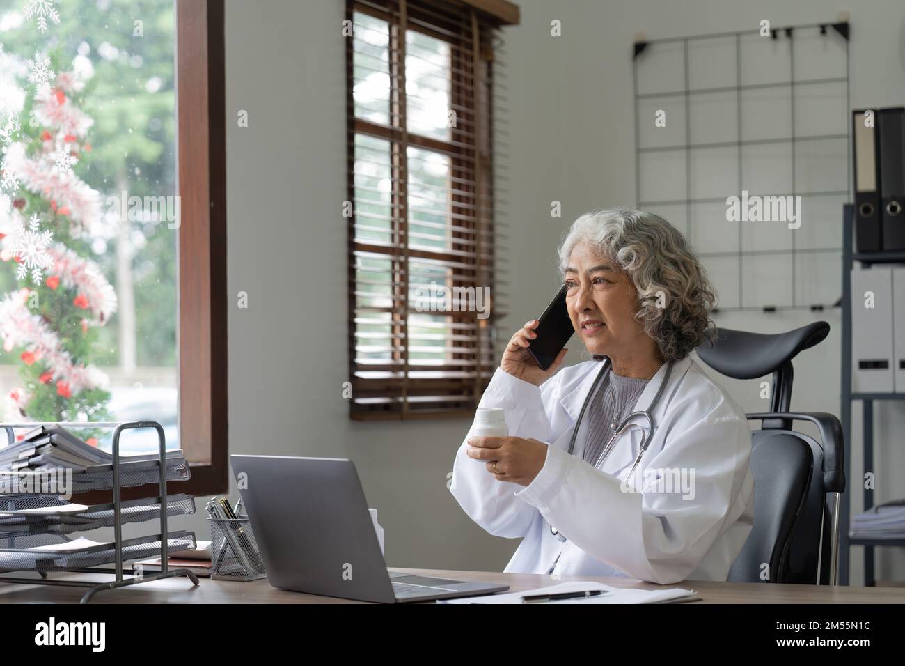Médecin asiatique senior utilisant un téléphone portable parlant alors qu'elle est assise dans le bureau de l'hôpital. femme heureuse médecin travailleur ayant une conversation joyeuse avec Banque D'Images