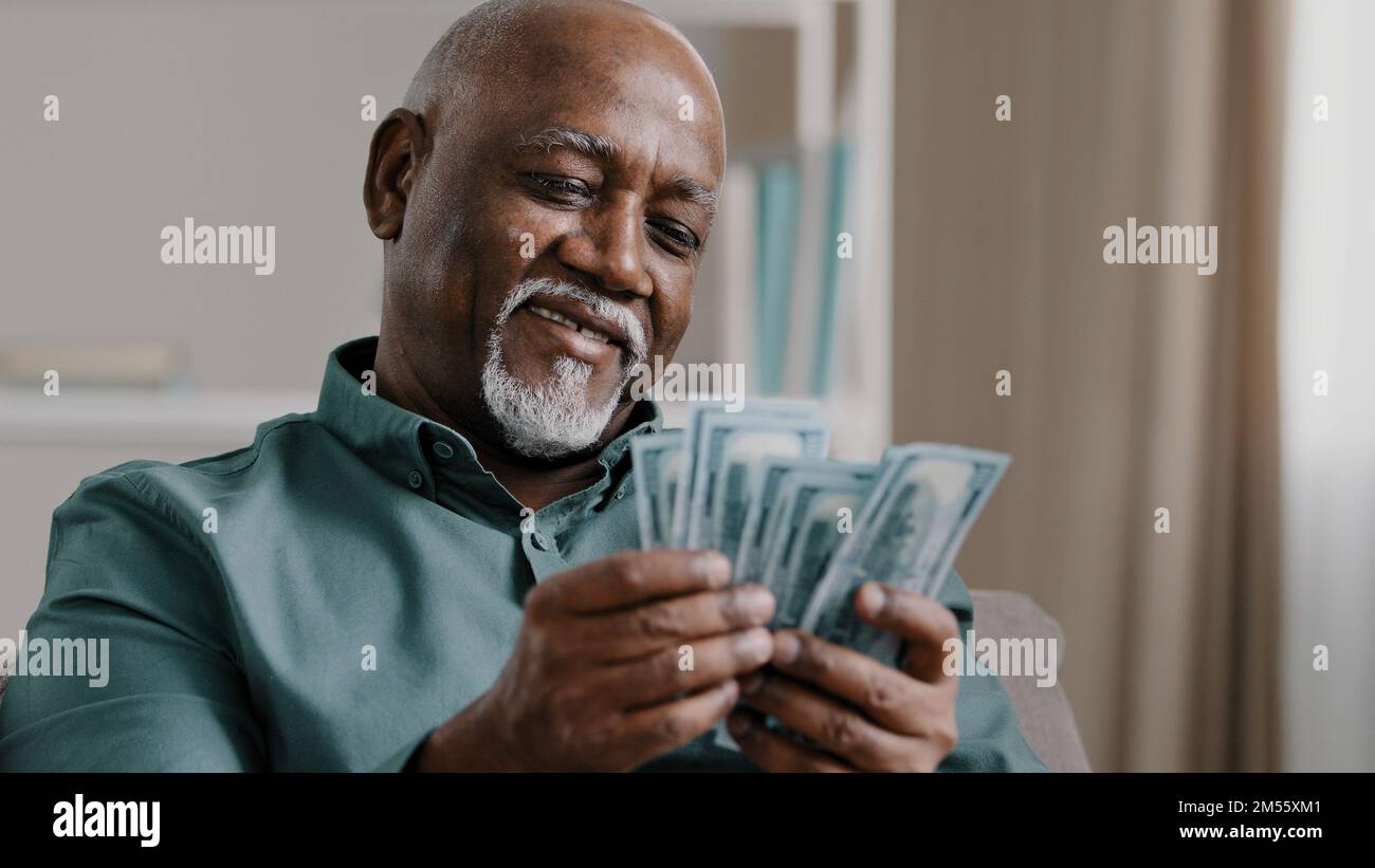 Joyeux afro-américain satisfait gagnant pari vieux retraité homme comptant épargne mature homme avec pile dollars comptage billets réussite Banque D'Images