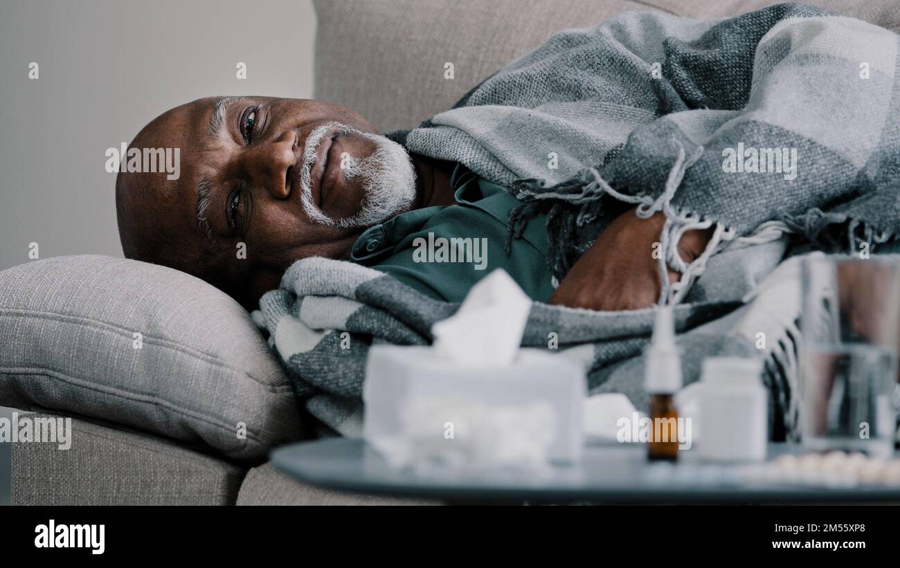 Vieux chauve barbu en surpoids homme d'âge moyen grand-père africain homme d'affaires malade allongé sur un canapé à la maison avec fièvre à haute température, maladie froide Banque D'Images