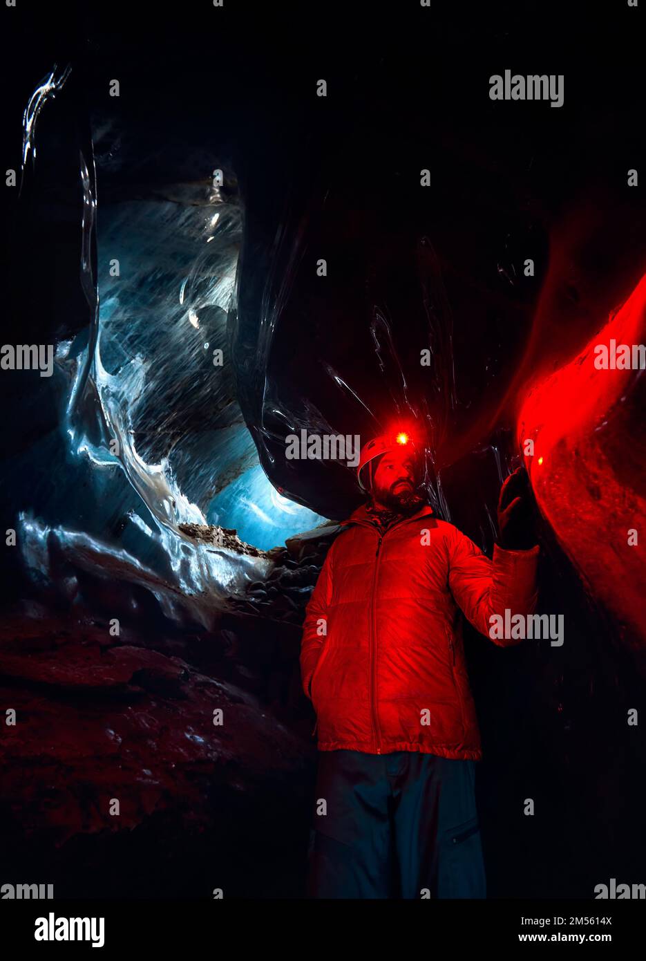 Silhouette de l'alpiniste dans un casque avec phare lumineux rouge dans une grotte de glace glaciaire profonde et étroite avec lumières cyan, explorez le glacier de montagne d'hiver au Kazakhstan Banque D'Images