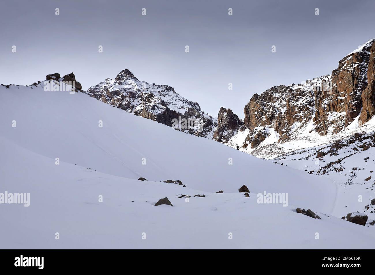 Skieur grimpant avec sac à dos et son ski dans les hautes montagnes enneigées et les pics rocheux. Sport en plein air en hiver. Banque D'Images