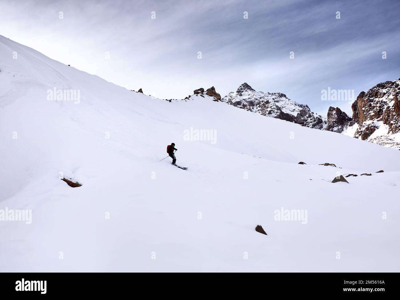 Skieur ski alpin avec sac à dos rouge dans un casque et un masque dans des montagnes enneigées. Sport en plein air en hiver. Banque D'Images